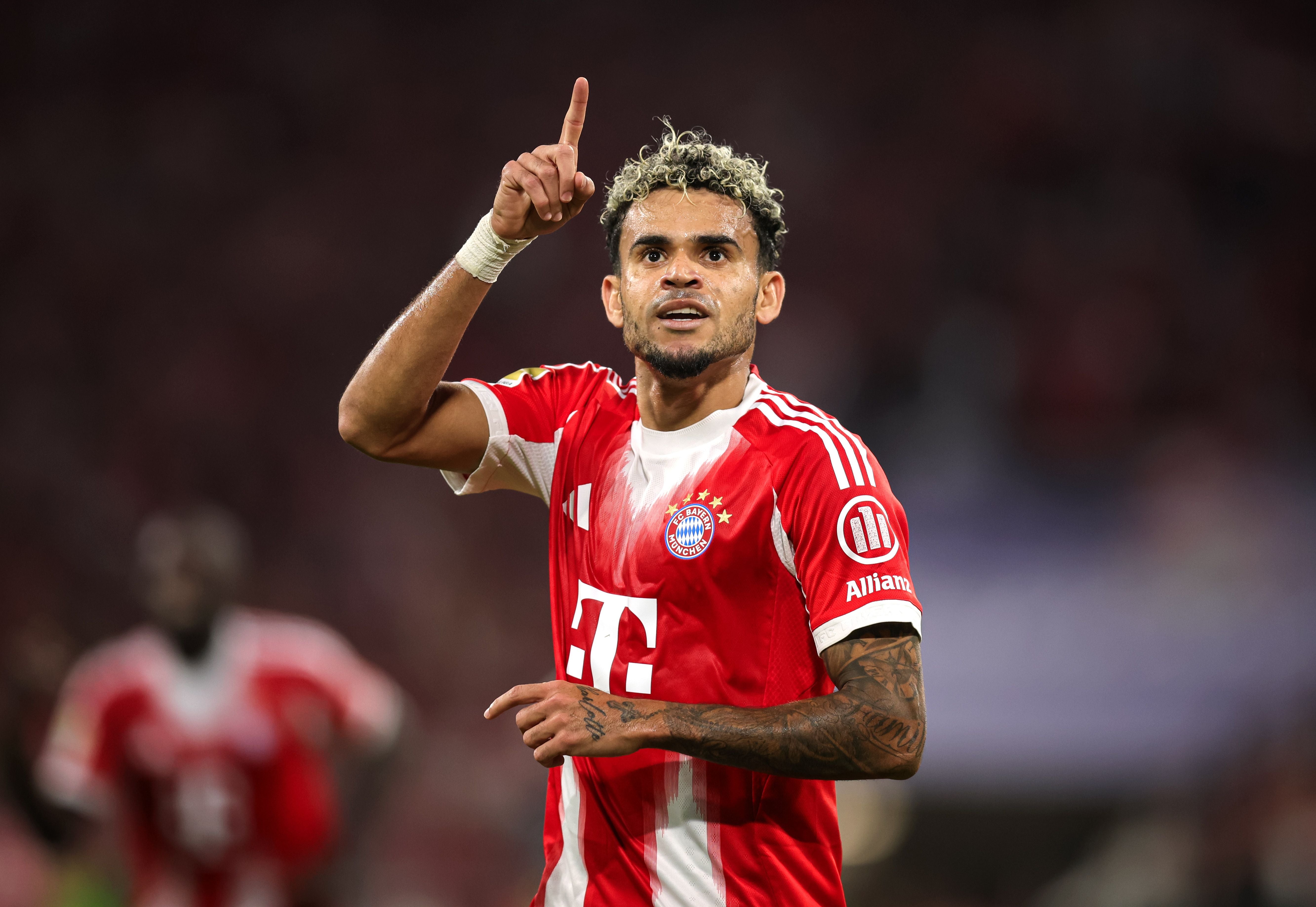 Ein Fußballspieler im roten Bayern-Trikot jubelt und zeigt mit dem Finger nach oben.