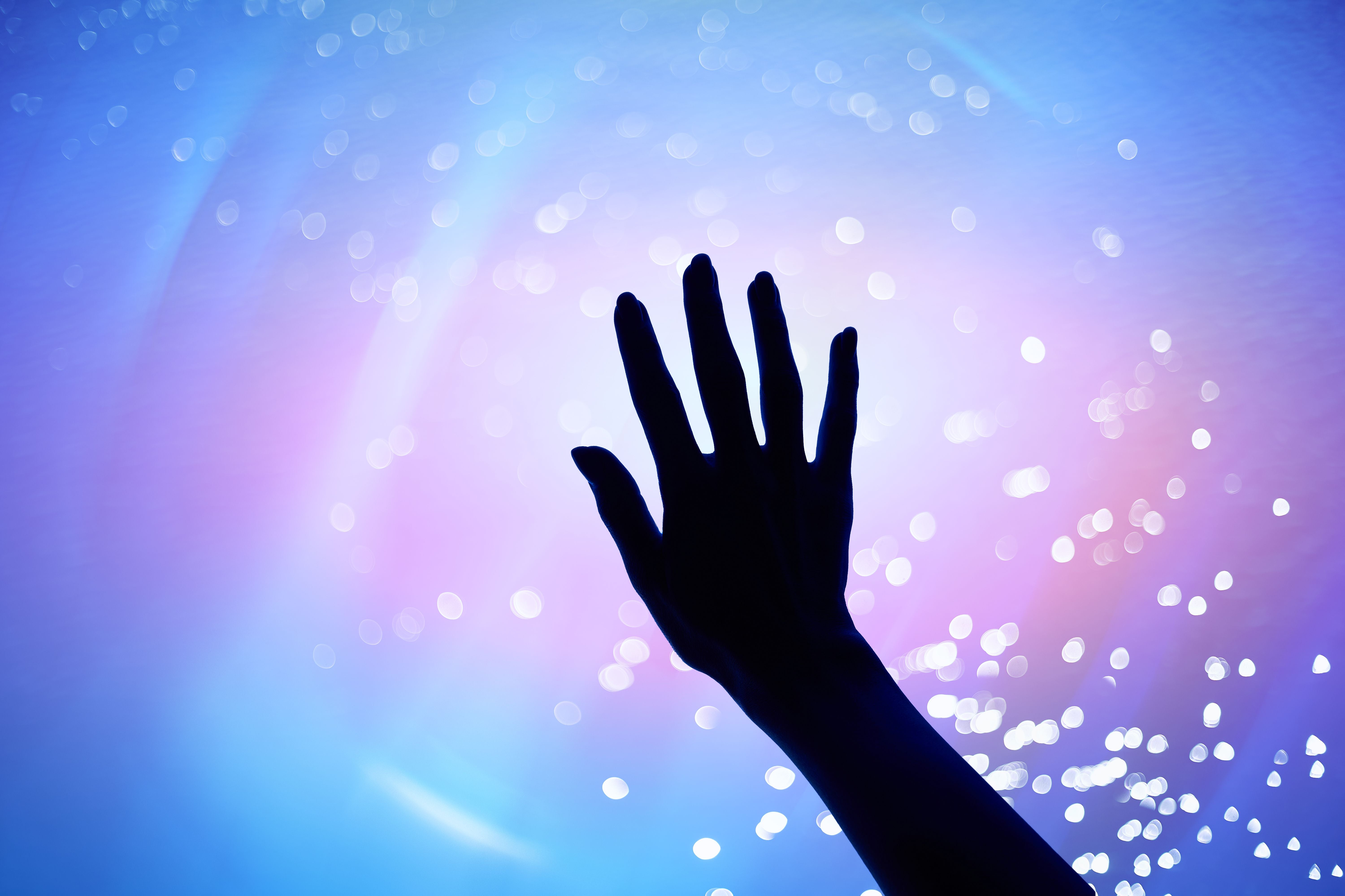 Eine menschliche Hand vor einem leuchtenden, neonfarbenen Hintergrund mit Lichtpunkten.