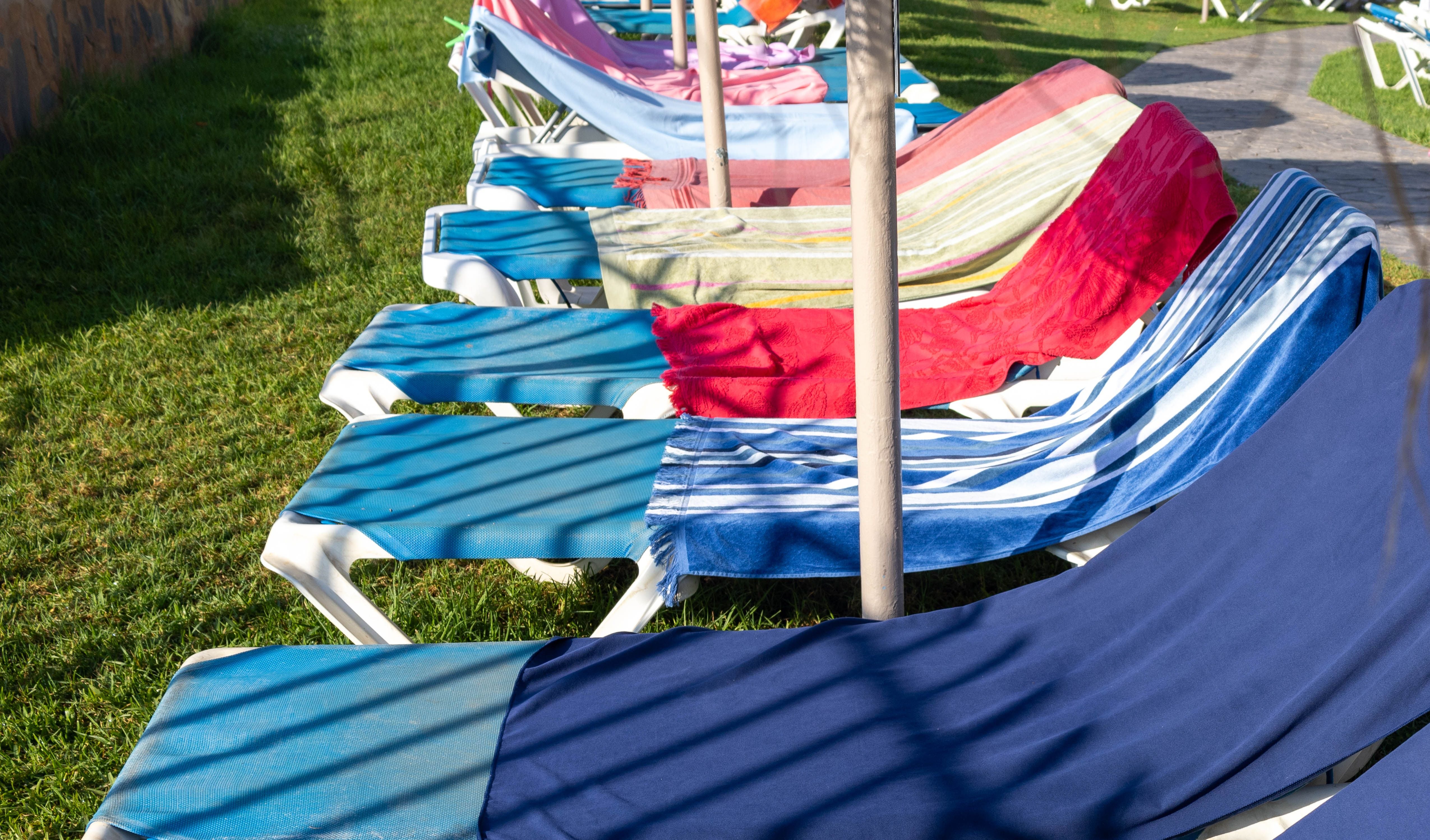 Mehrere Sonnenliegen am Pool mit bunten Handtüchern zur Reservierung belegt.