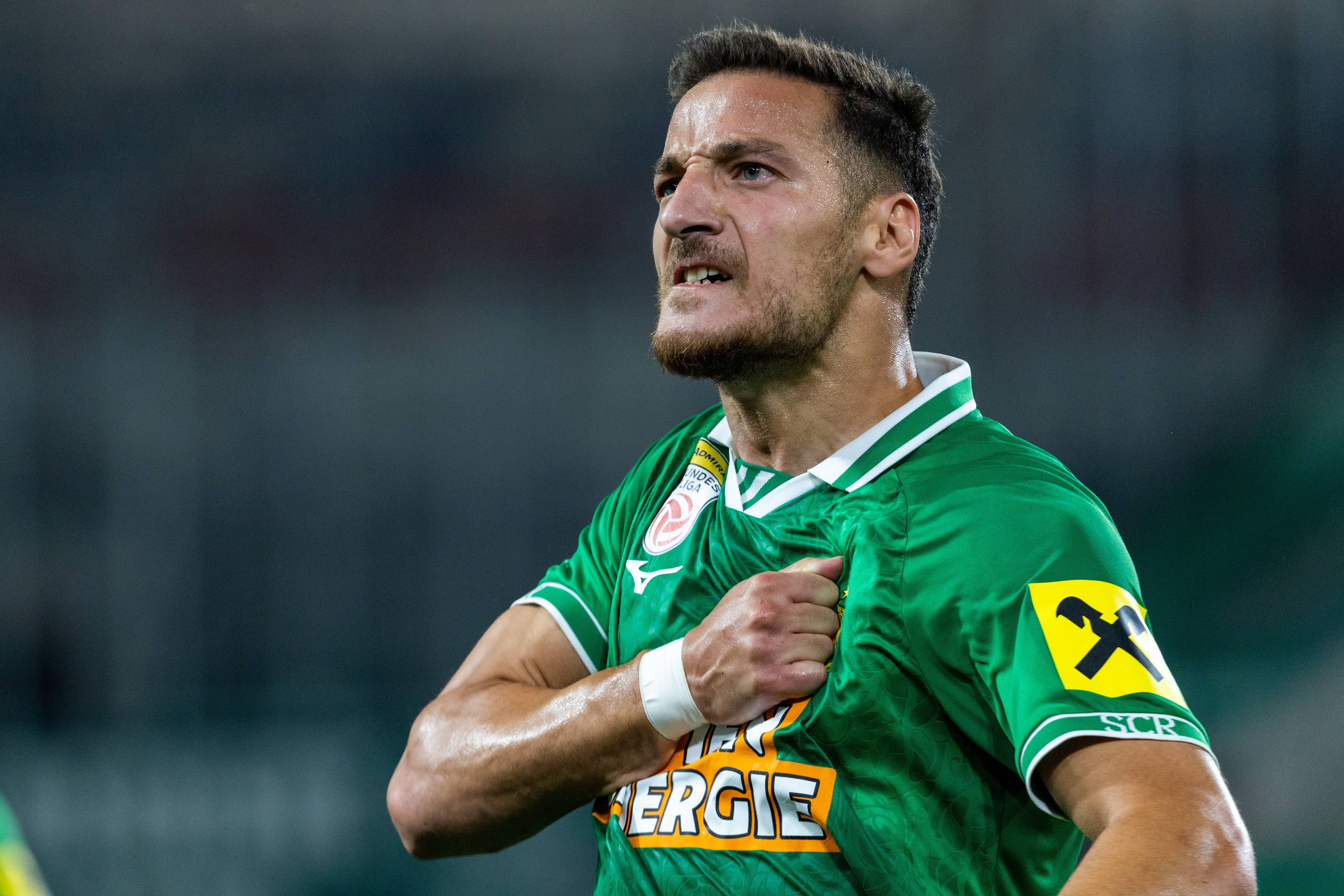Ein Fußballspieler im grünen Trikot jubelt mit der Hand auf der Brust.