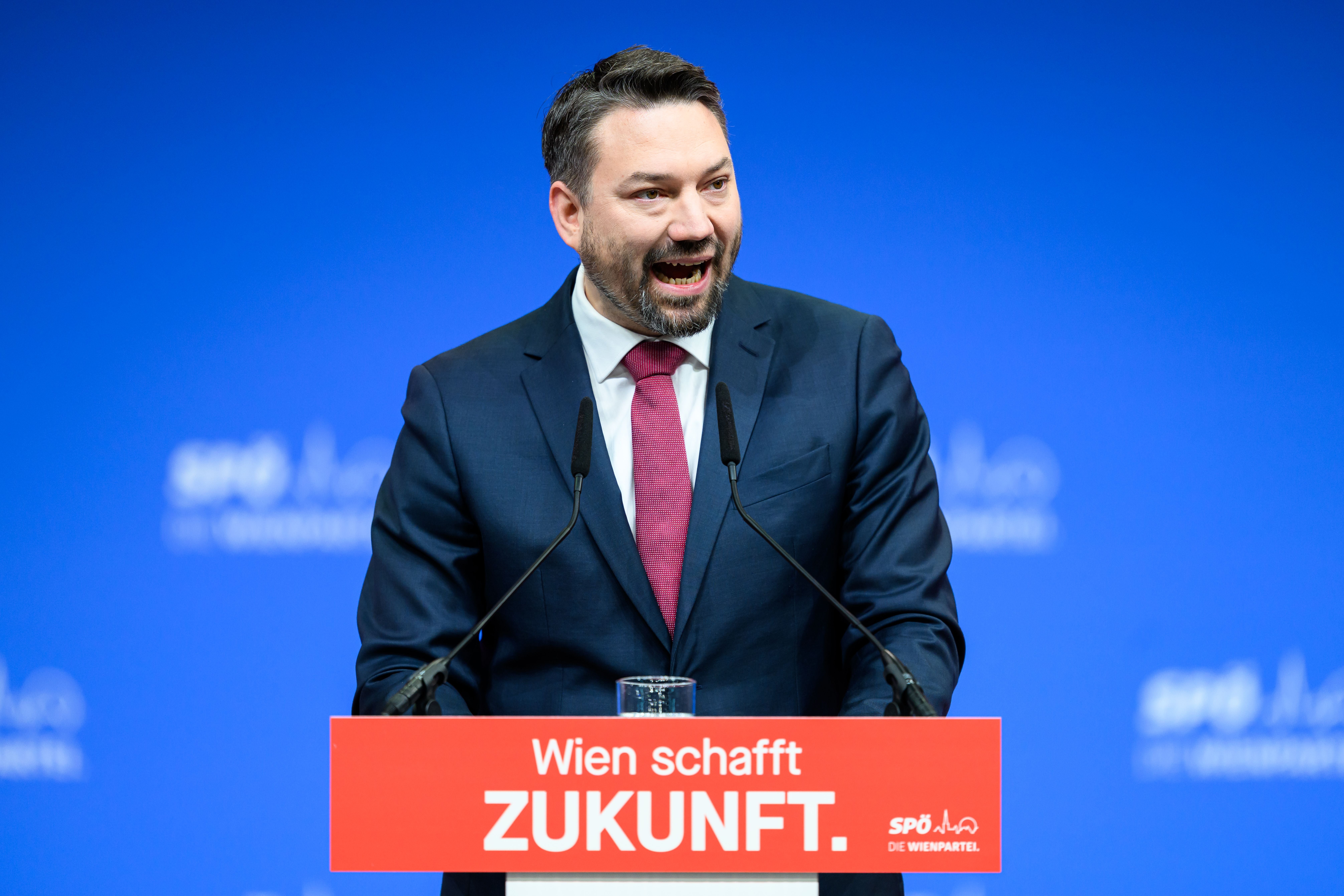 Ein Mann im Anzug spricht am Rednerpult vor blauem Hintergrund, Schriftzug: Wien schafft Zukunft.