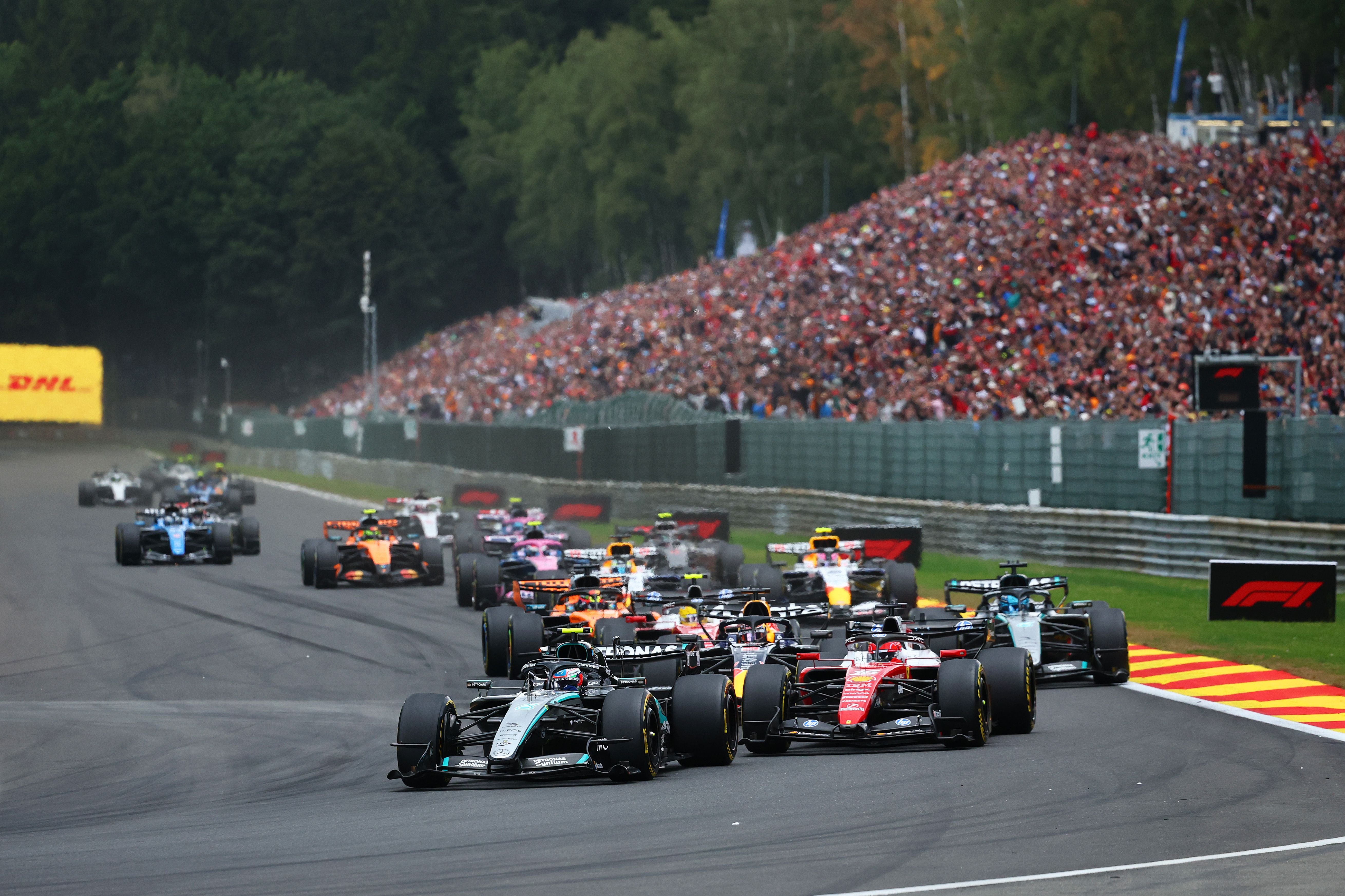 Formel-1-Rennstart in Spa mit mehreren Autos auf der Strecke und Zuschauern im Hintergrund.