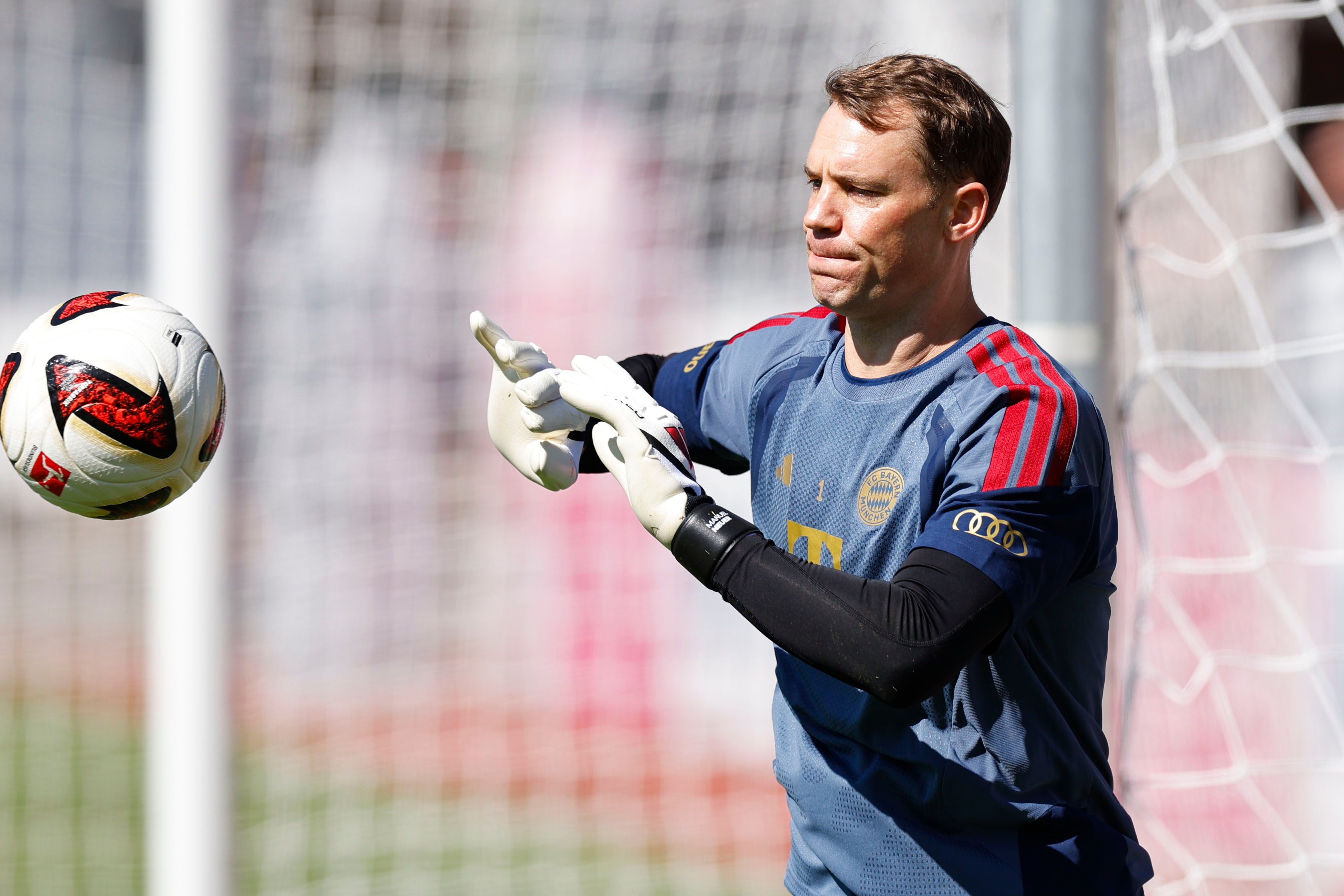Ein Torwart im Bayern-Trikot trainiert mit einem Ball vor dem Tor bei Sonnenschein.