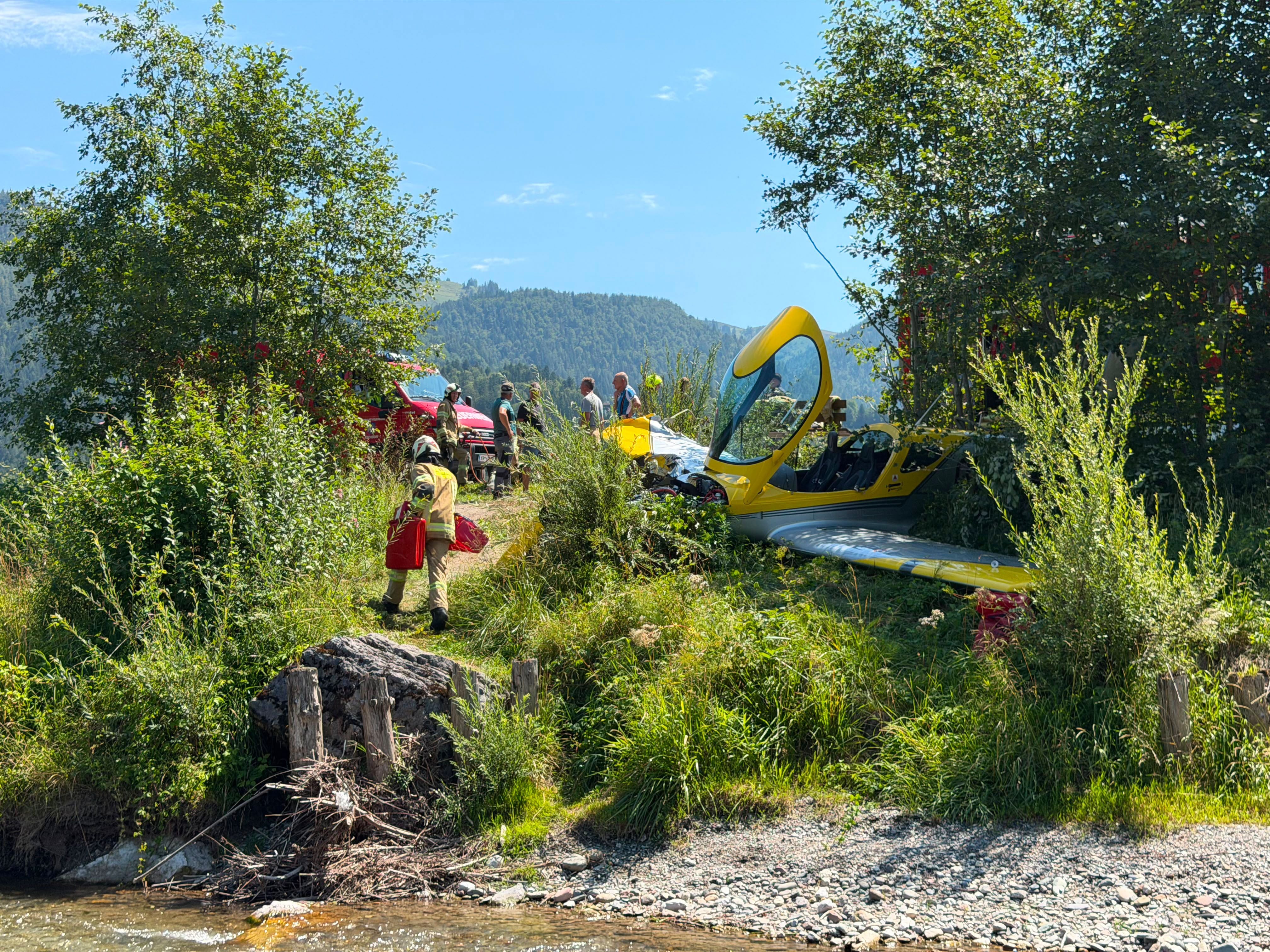 Ein gelbes Kleinflugzeug ist im Grünen neben einem Bach verunglückt, Feuerwehrleute sind vor Ort.