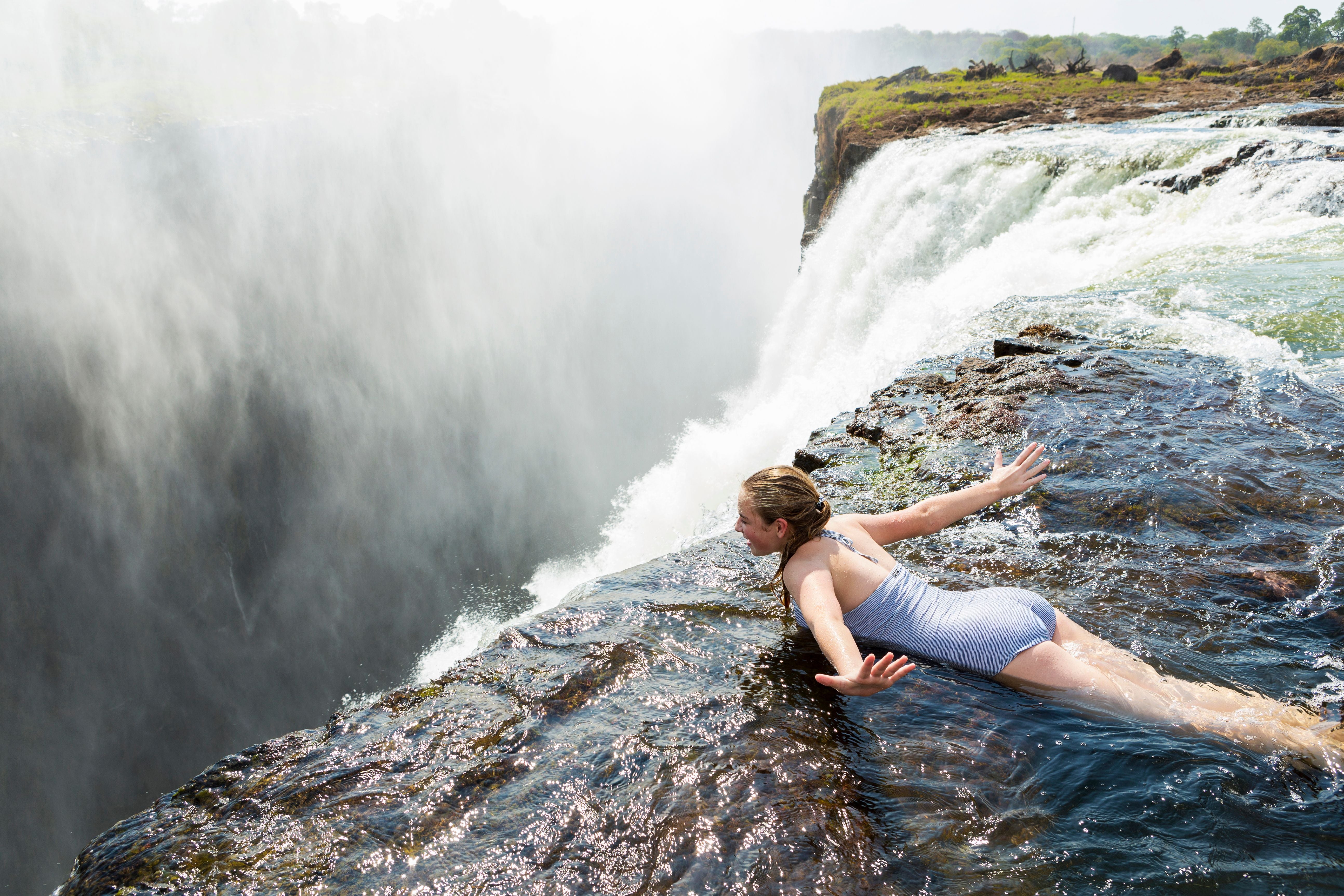 Frau liegt am Rand des Devils Pool am Wasserfall, direkt neben der Abbruchkante.