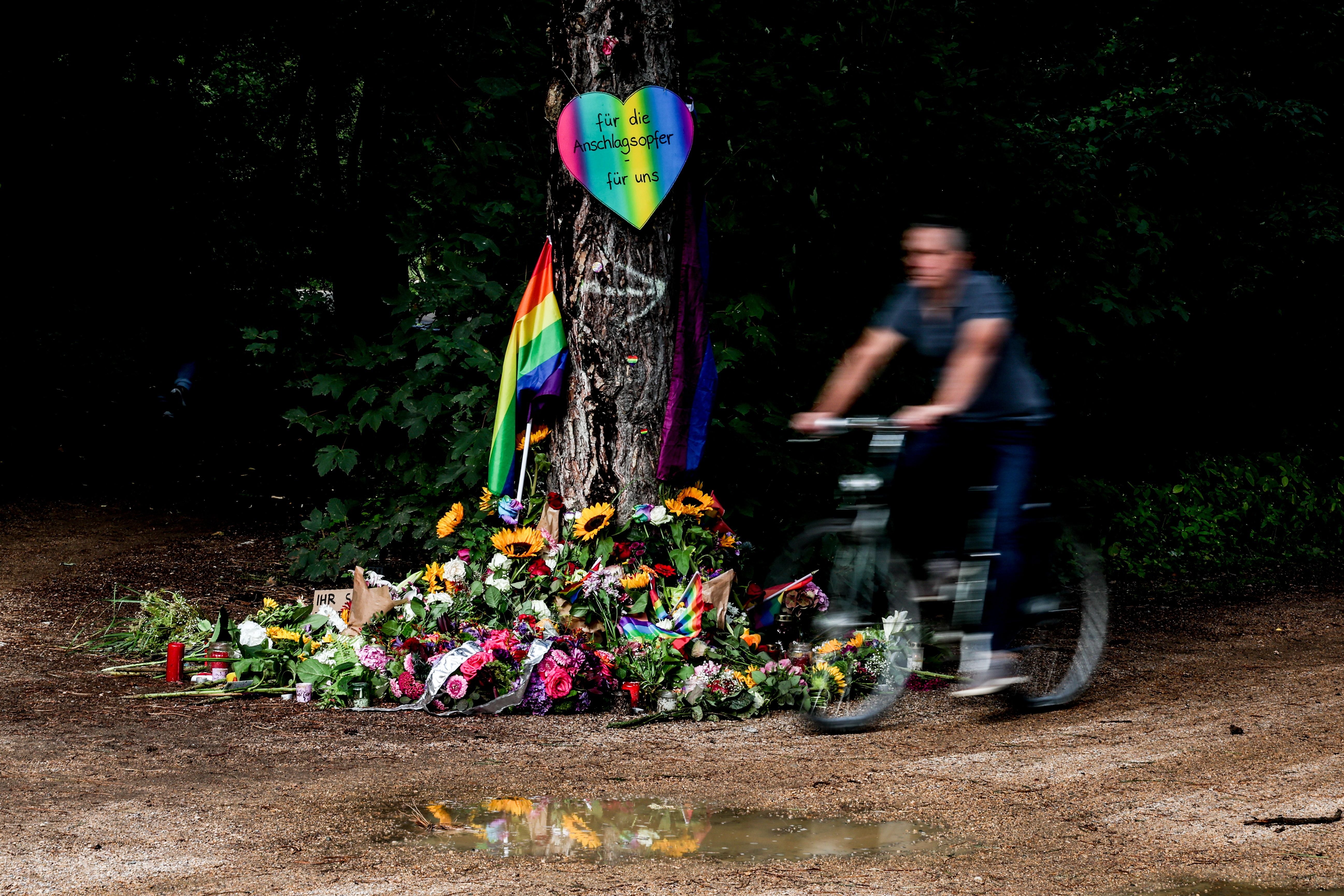 Ein Radfahrer fährt an einer Gedenkstätte mit Regenbogenflagge und Blumen vorbei.