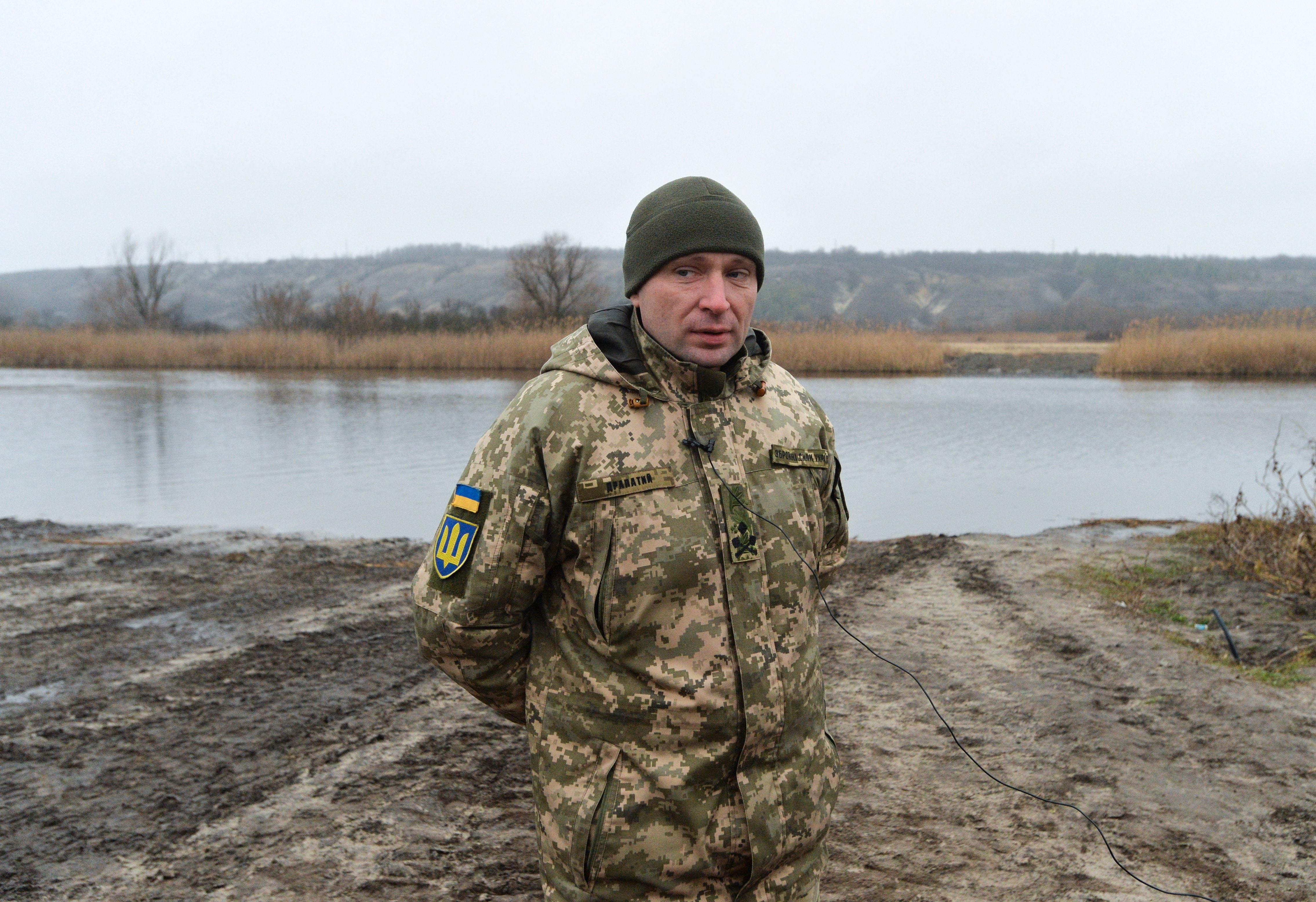 Ein Soldat in Tarnuniform steht an einem Flussufer bei bewölktem Wetter.