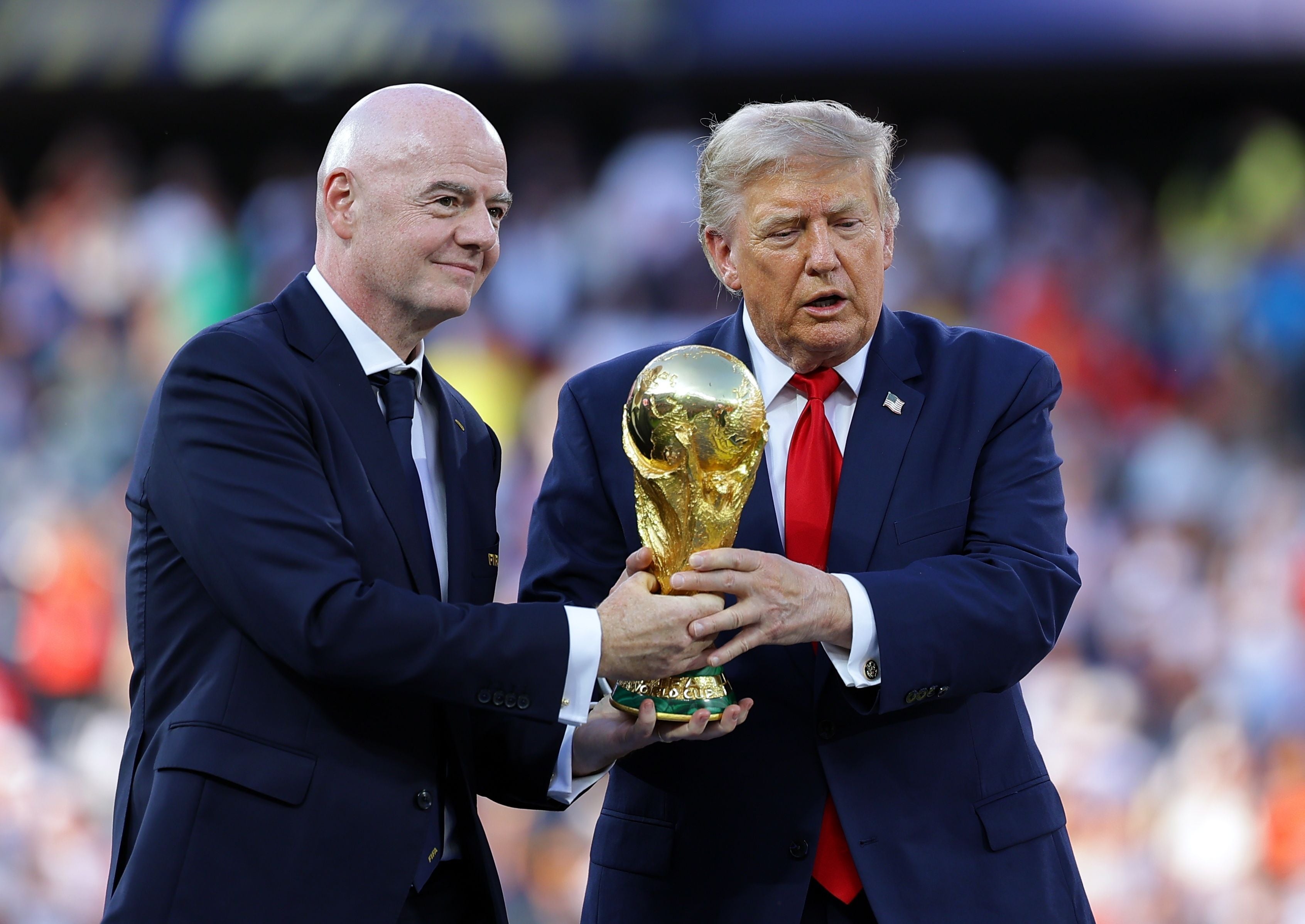Zwei Männer im Anzug halten gemeinsam den FIFA-Weltpokal bei einer Zeremonie.