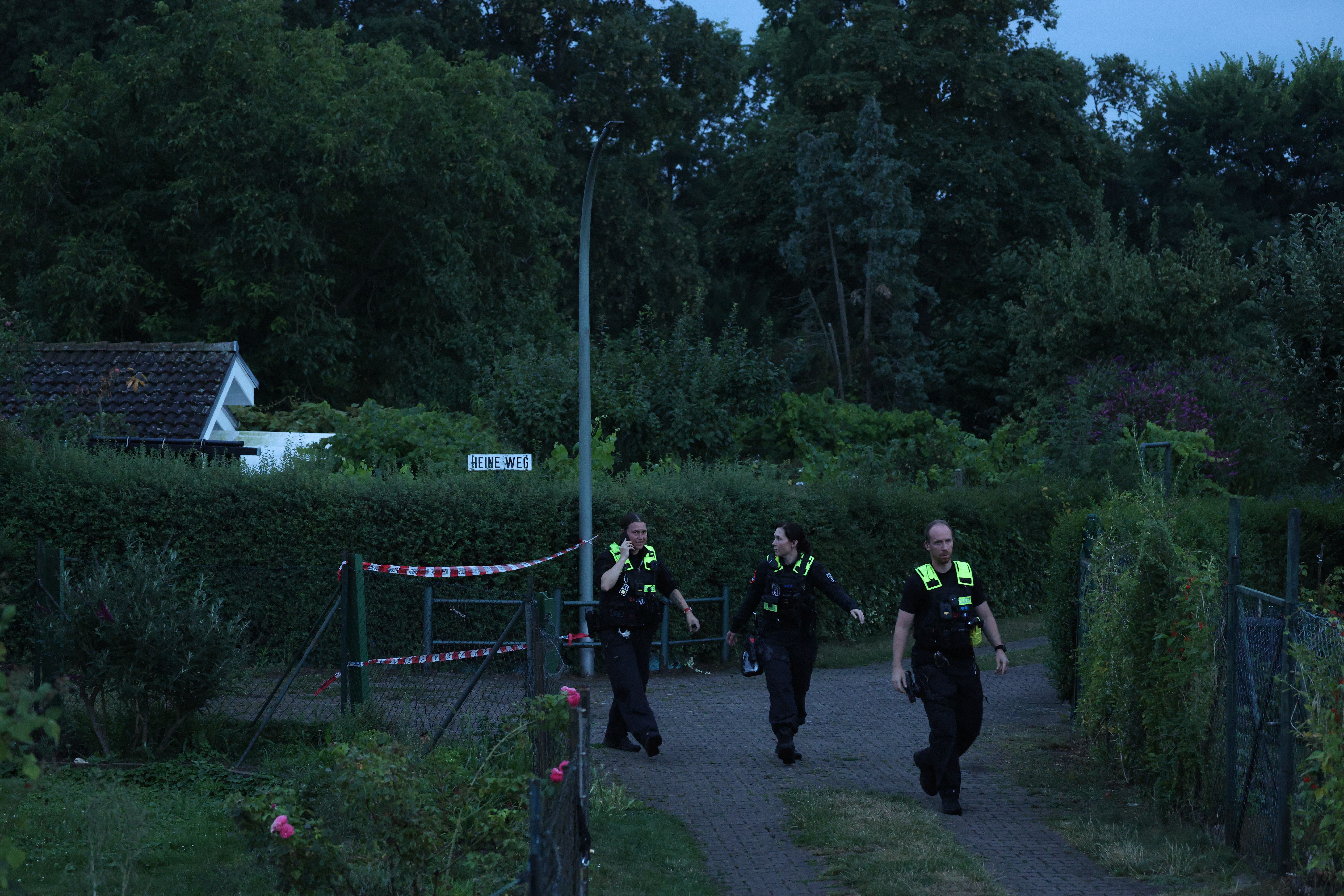 Drei Polizisten gehen durch eine Kleingartenanlage am Abend in Berlin-Spandau.