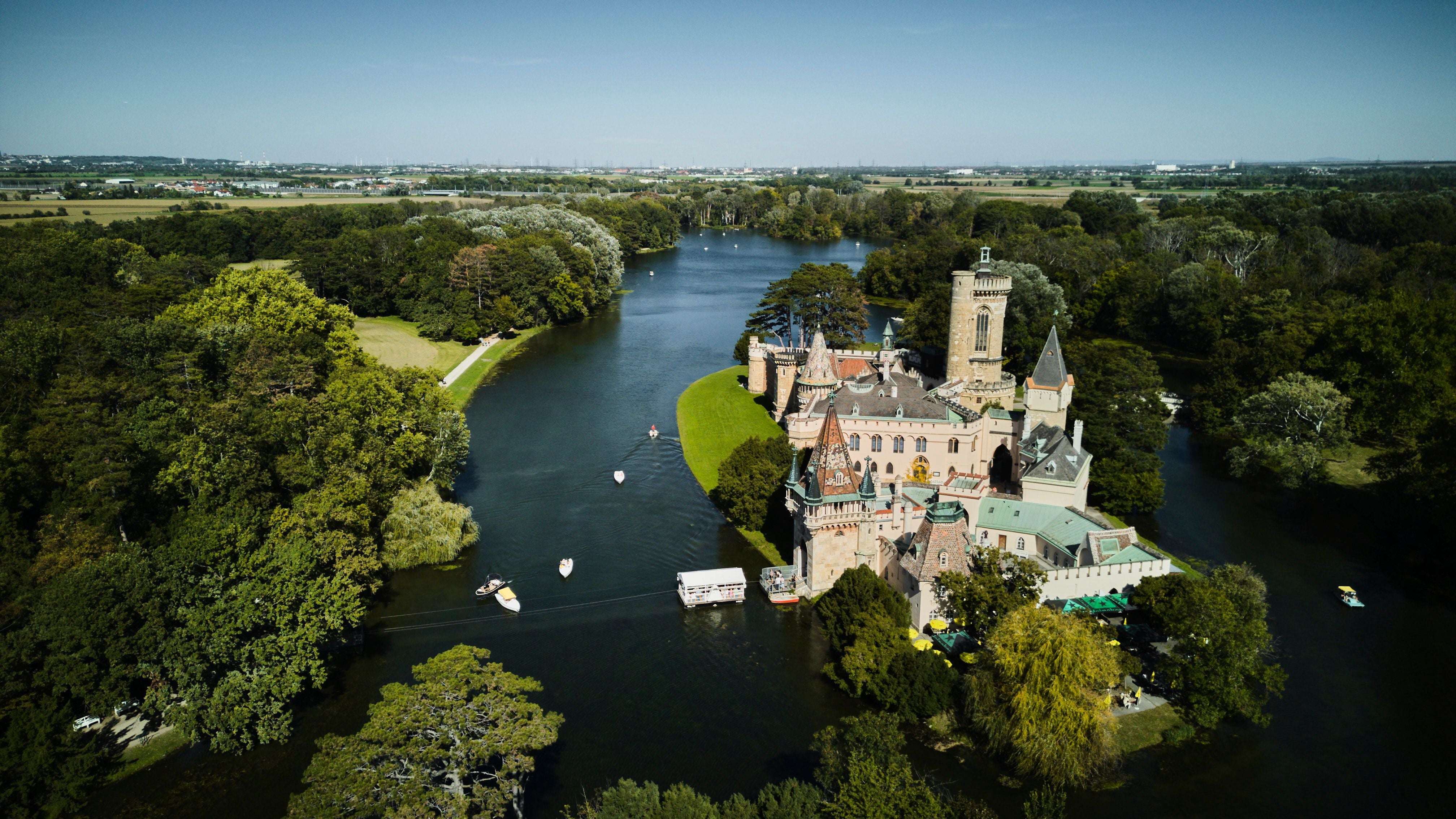 Luftaufnahme eines Schlosses auf einer Insel, umgeben von Fluss und viel Wald.