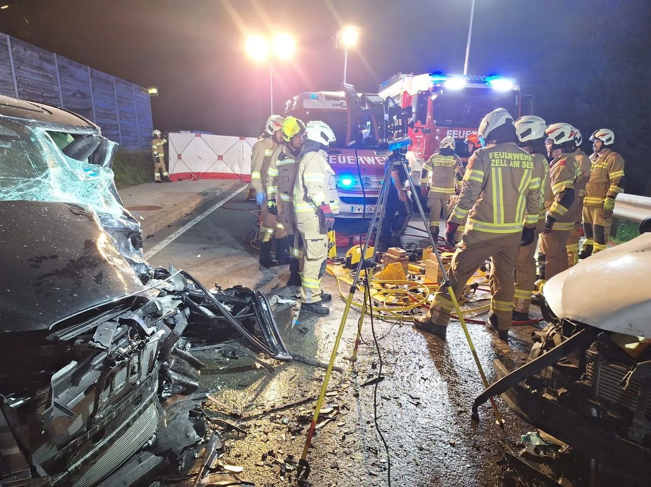 Feuerwehrleute arbeiten nachts an der Unfallstelle mit zwei stark beschädigten Autos.