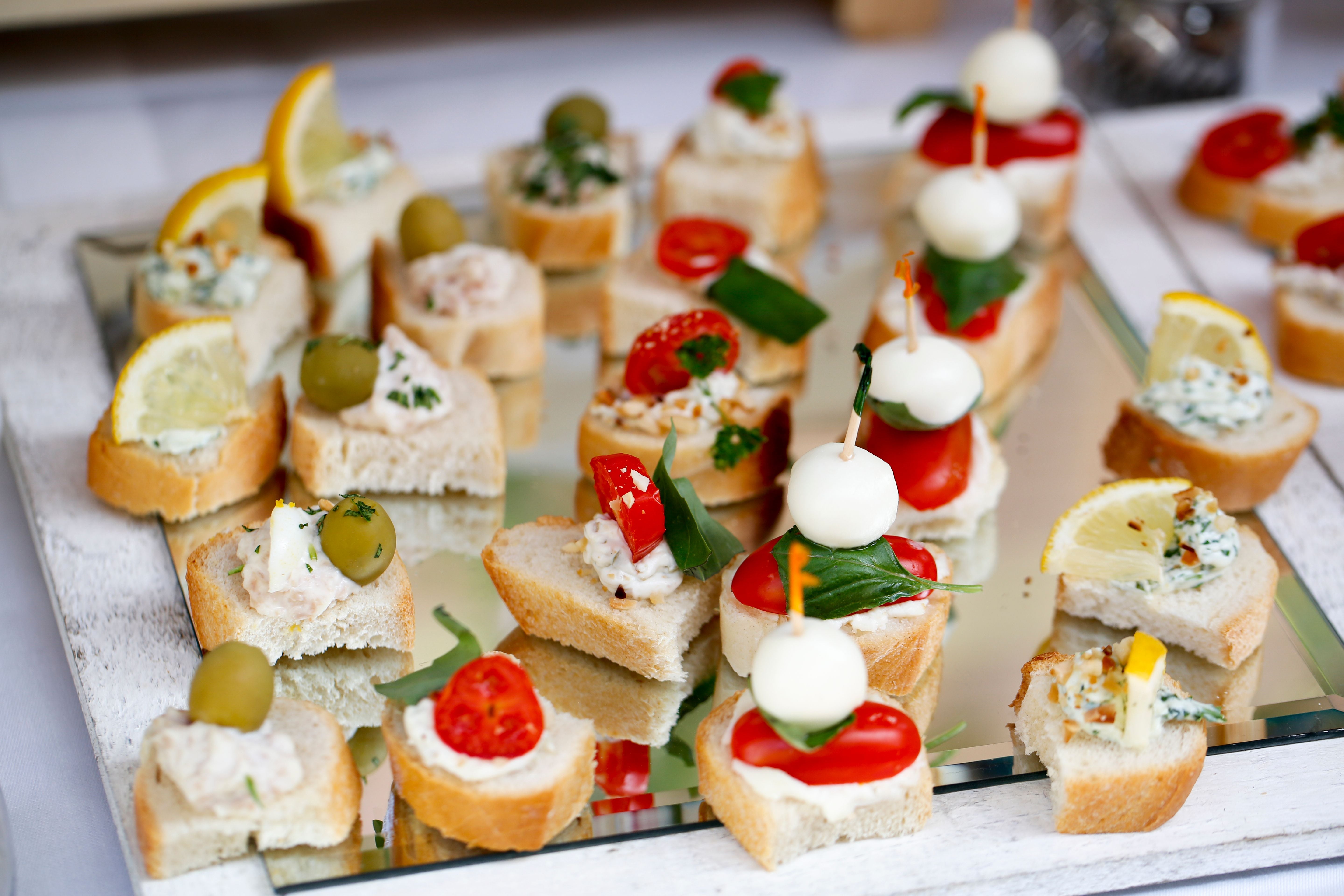 Verschiedene Canapés mit Käse, Tomaten, Oliven und Zitronen auf einem Spiegel serviert.
