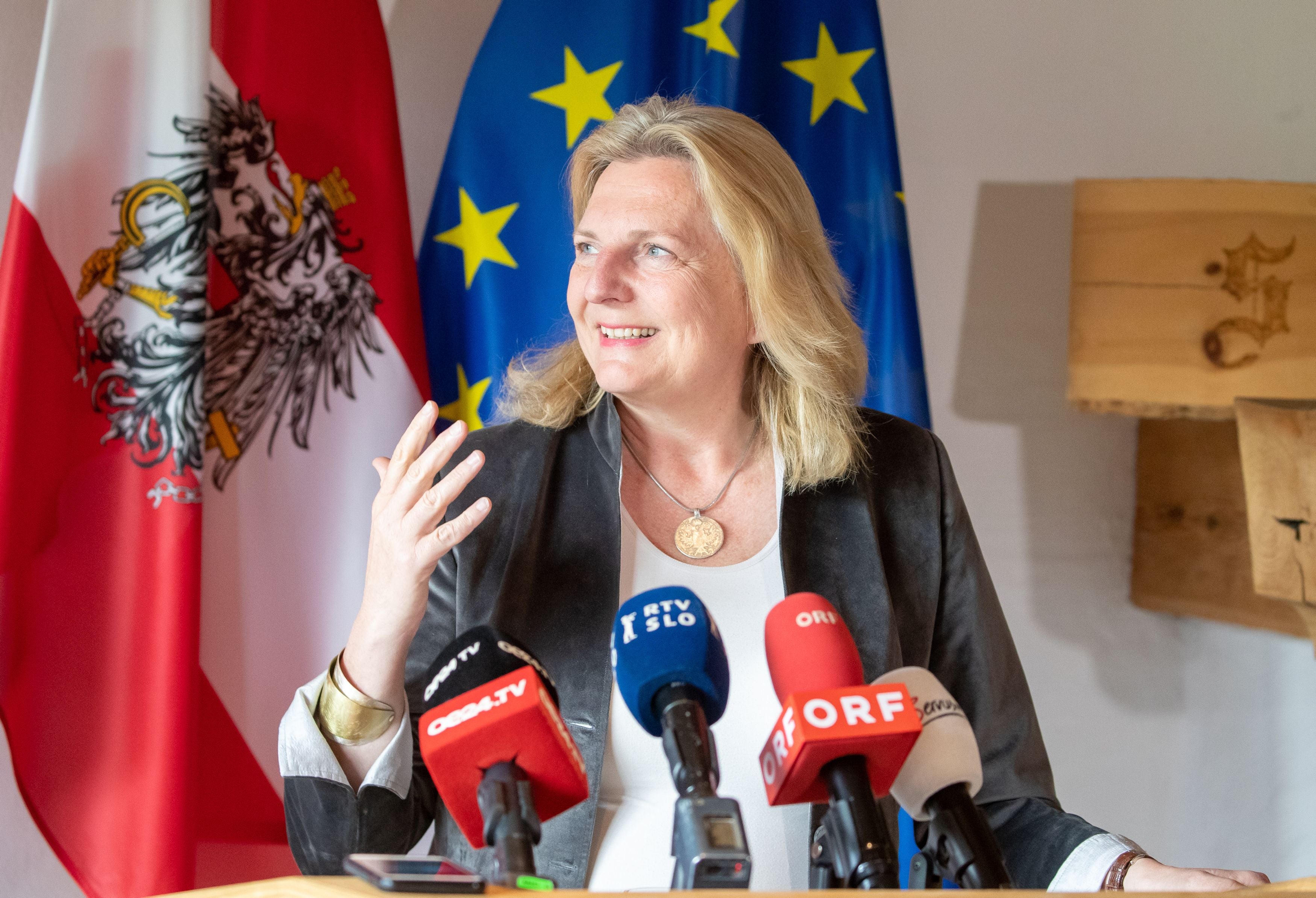 Österreichs Außenministerin spricht bei einer Pressekonferenz vor Mikrofonen und Flaggen.