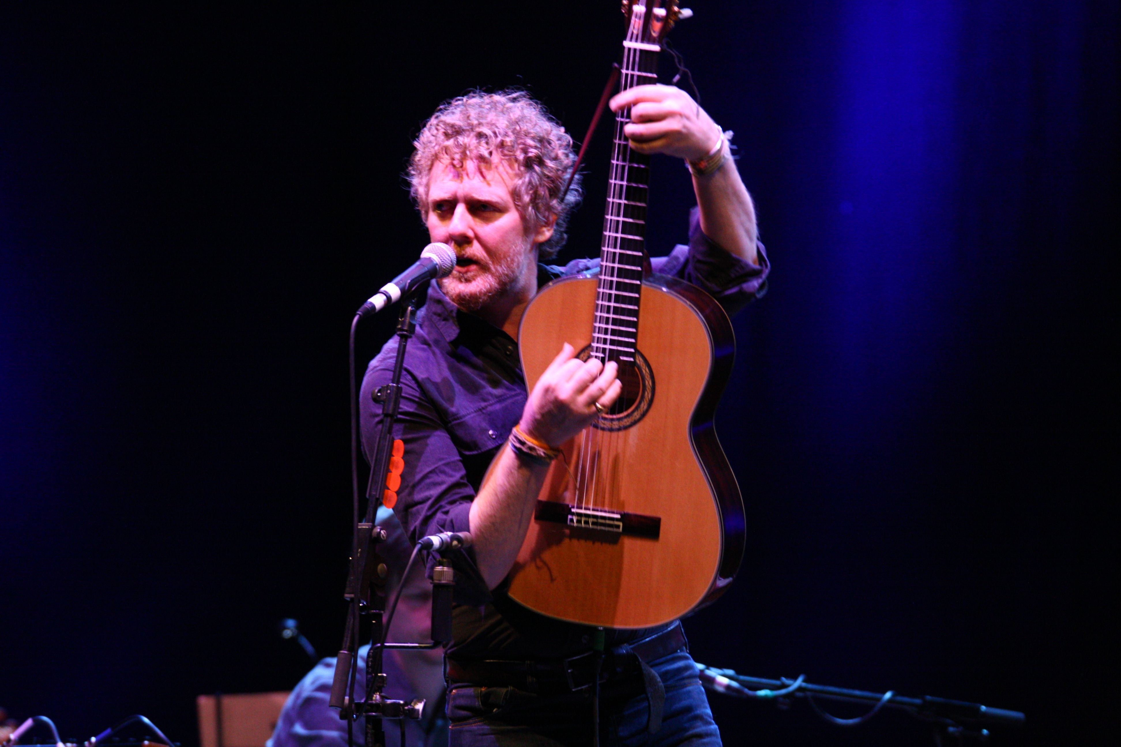 Mann mit Gitarre singt auf einer Bühne unter blauem Licht.