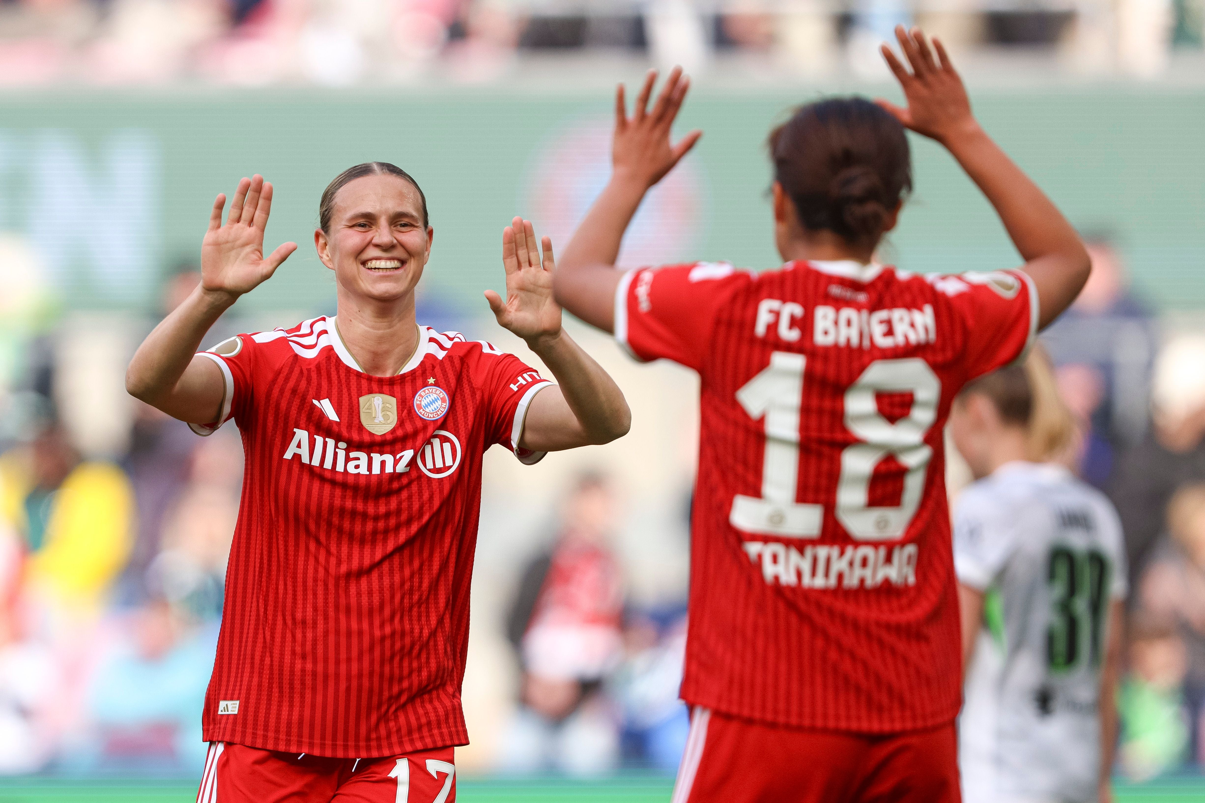 Zwei Spielerinnen des FC Bayern feiern im roten Trikot mit High-Five auf dem Fußballfeld.