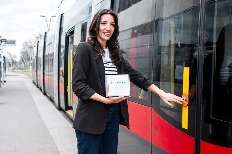 Frau hält ein Paket und drückt den Türöffner an einer roten Straßenbahn.