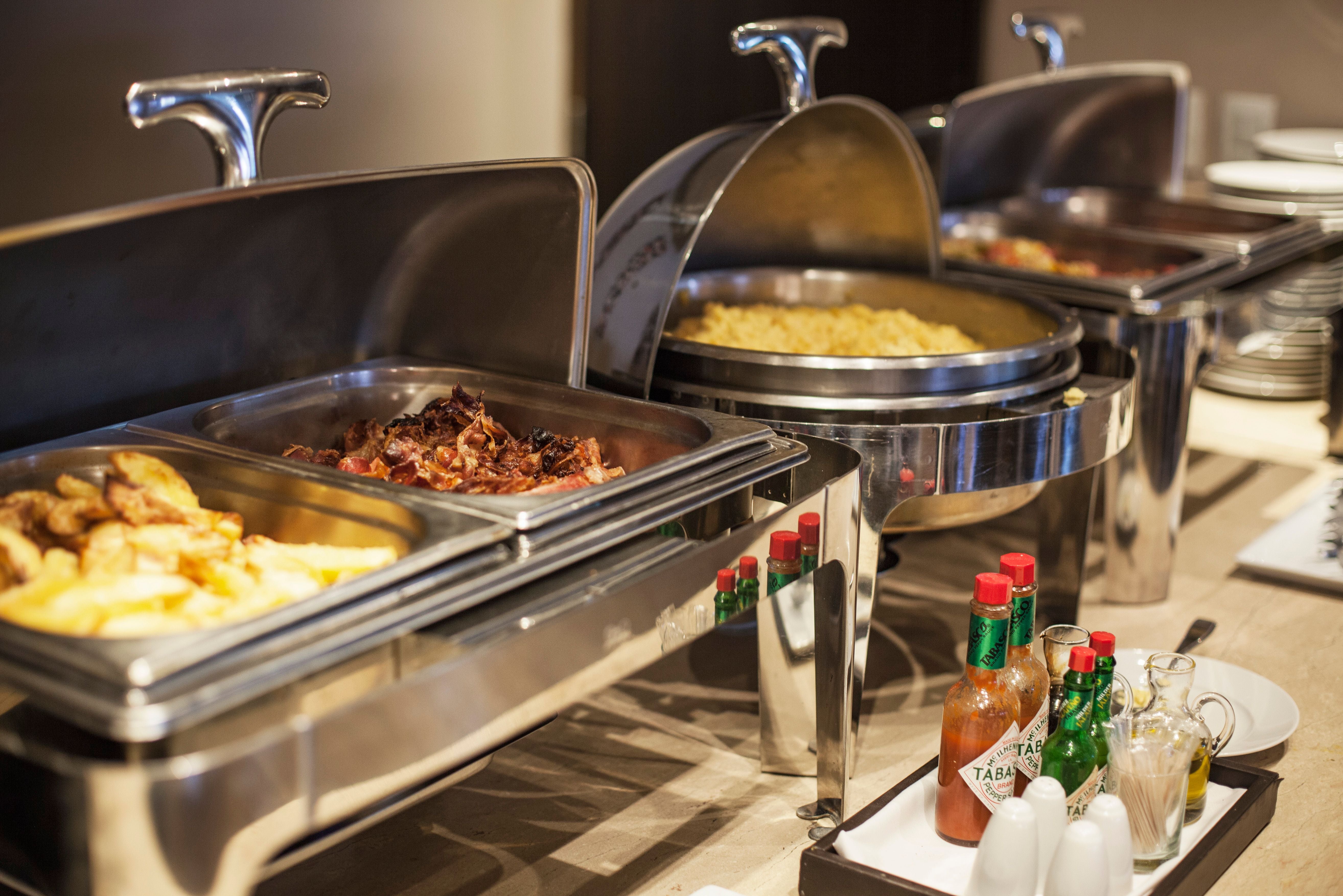 Buffet mit verschiedenen warmen Speisen und Gewürzen wie Tabasco-Soße auf dem Tisch.