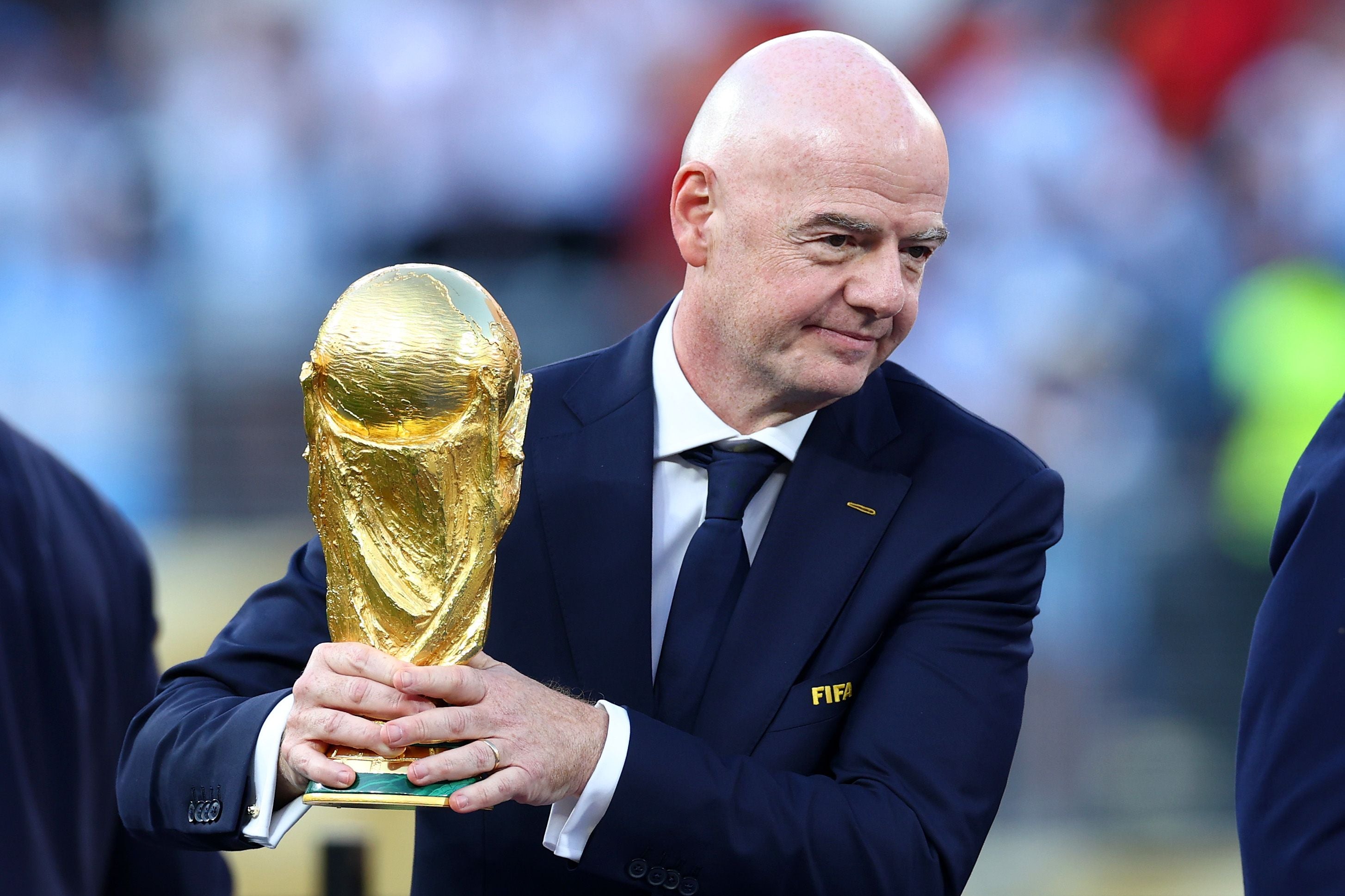 Ein Mann im Anzug hält den FIFA-WM-Pokal in den Händen.