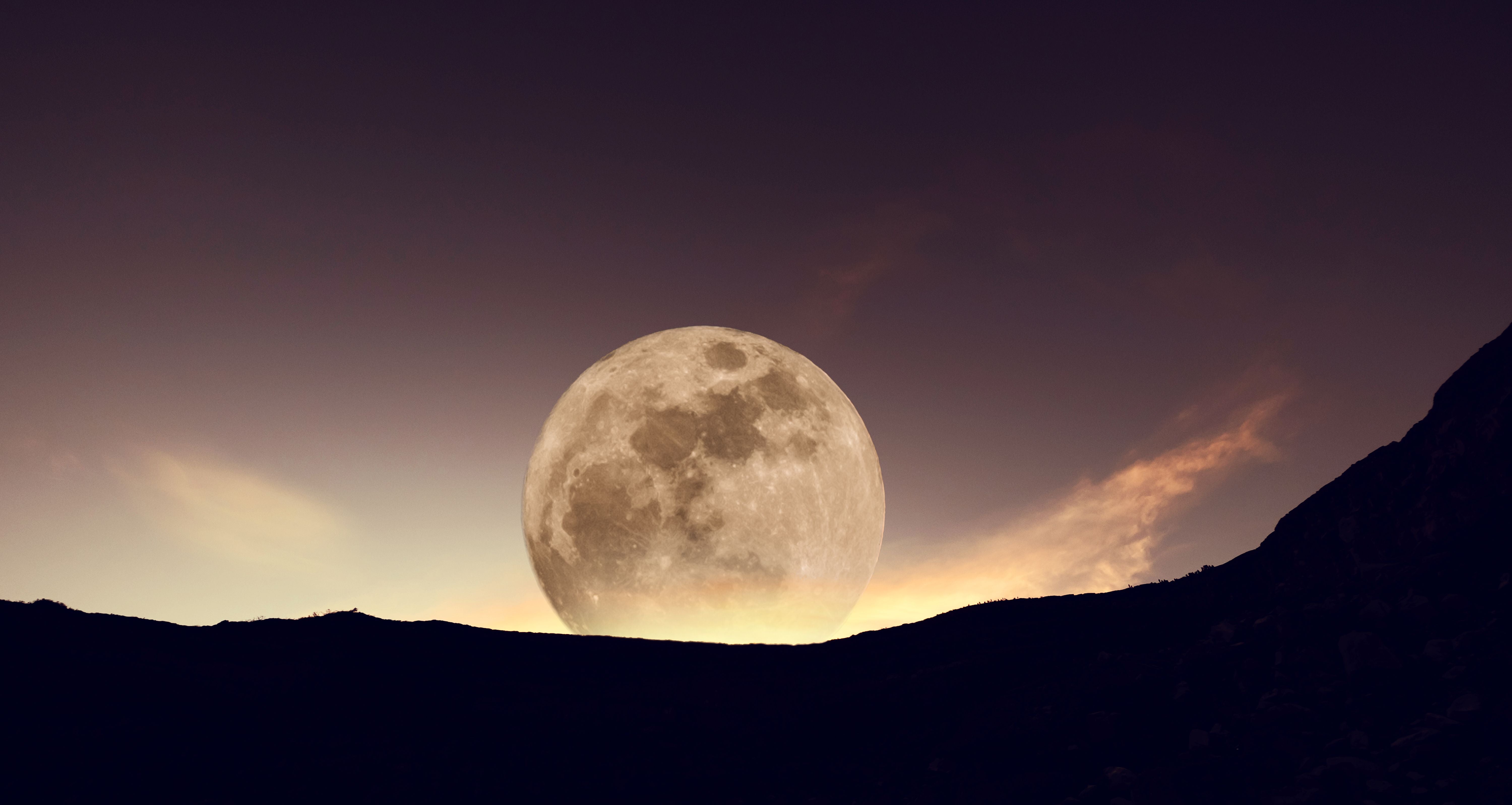 Vollmond geht hinter einem Berg im Morgengrauen auf.