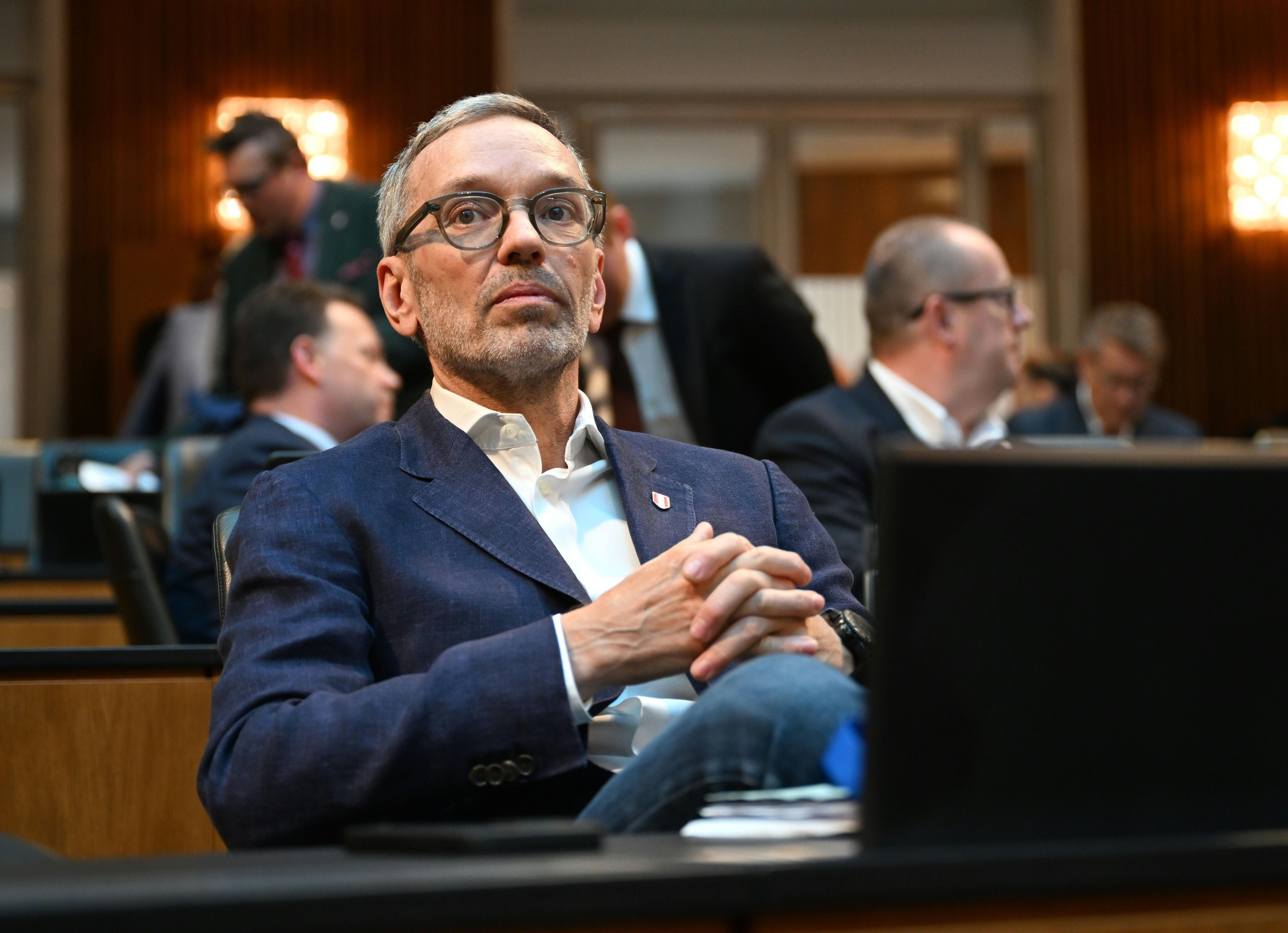 Ein Mann mit Brille und blauem Sakko sitzt nachdenklich in einem Sitzungssaal.