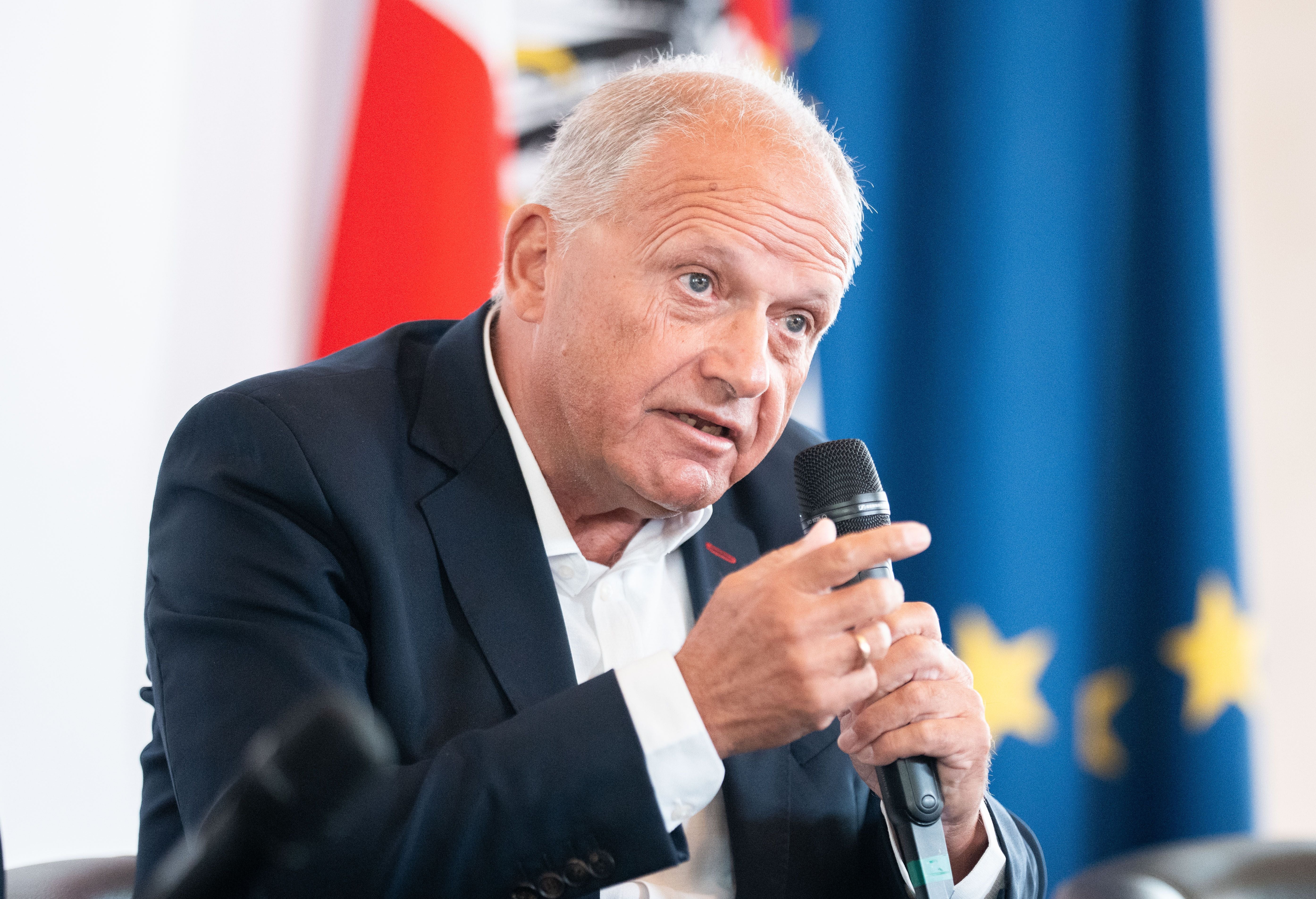 Ein Mann im Anzug spricht bei einer Veranstaltung mit einem Mikrofon in der Hand.