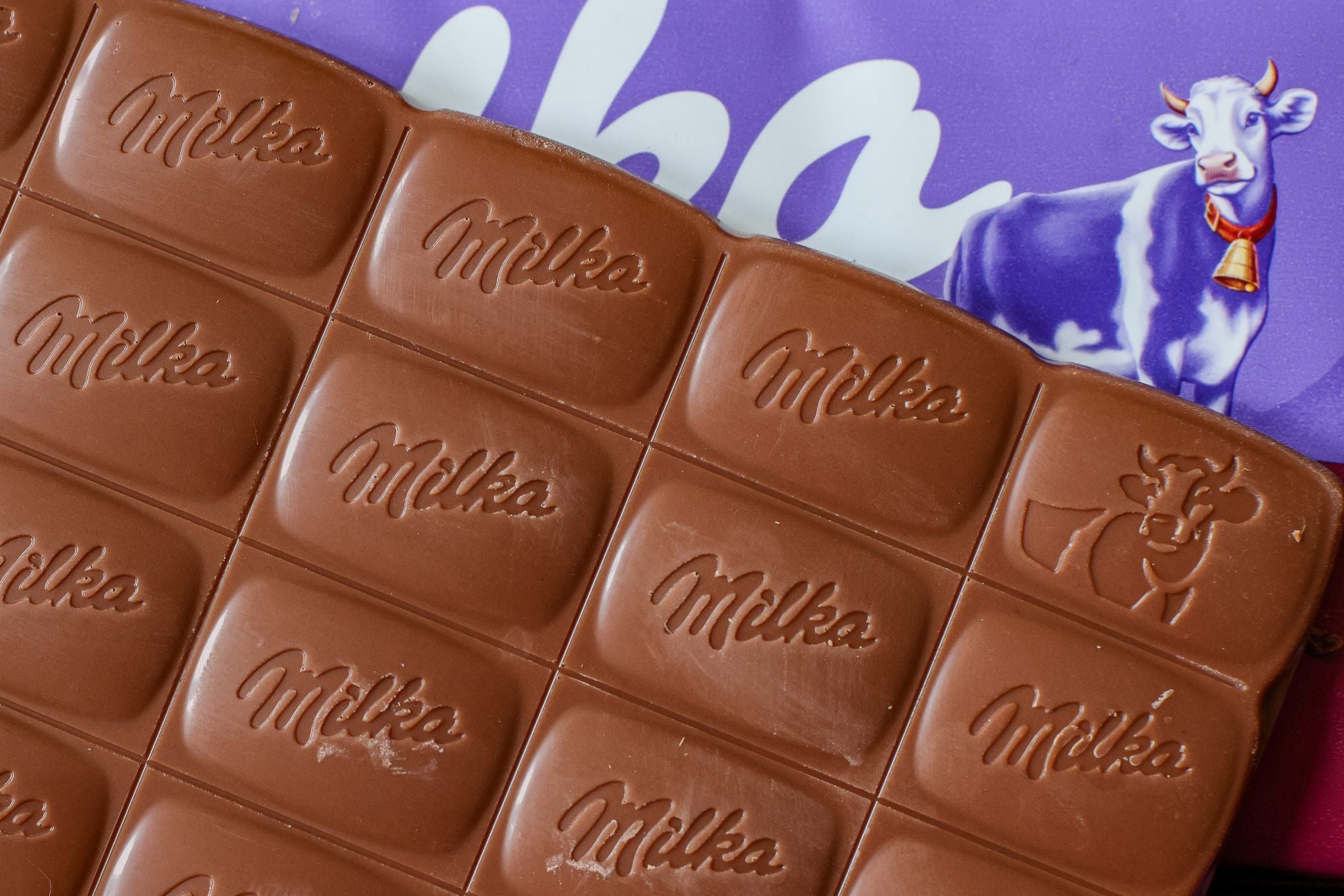 Eine angebrochene Milka Alpenmilch-Schokoladentafel liegt auf ihrer lila Verpackung.