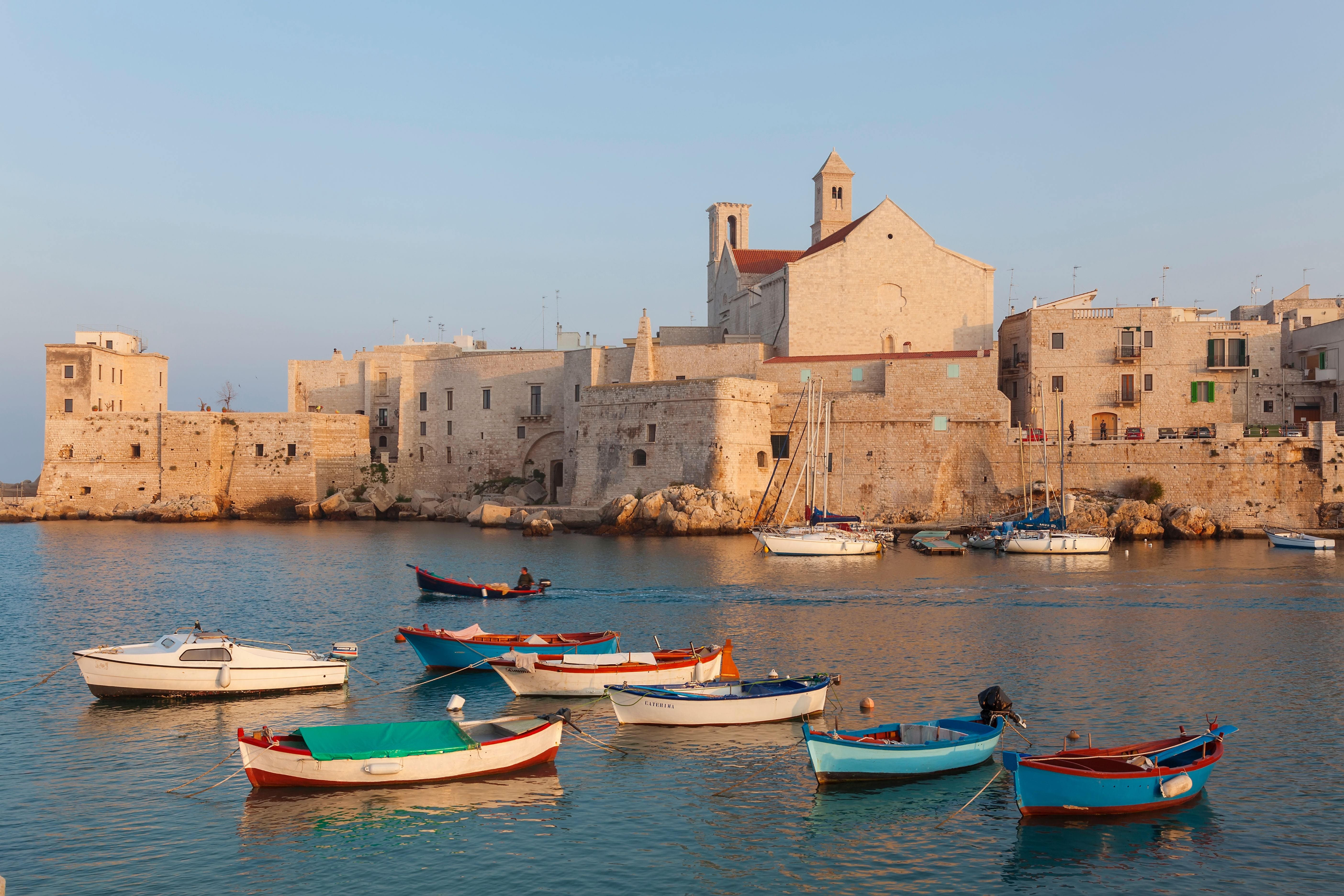 Bunte Boote liegen im Hafen von Giovinazzo vor historischen Gebäuden in Puglia, Italien.