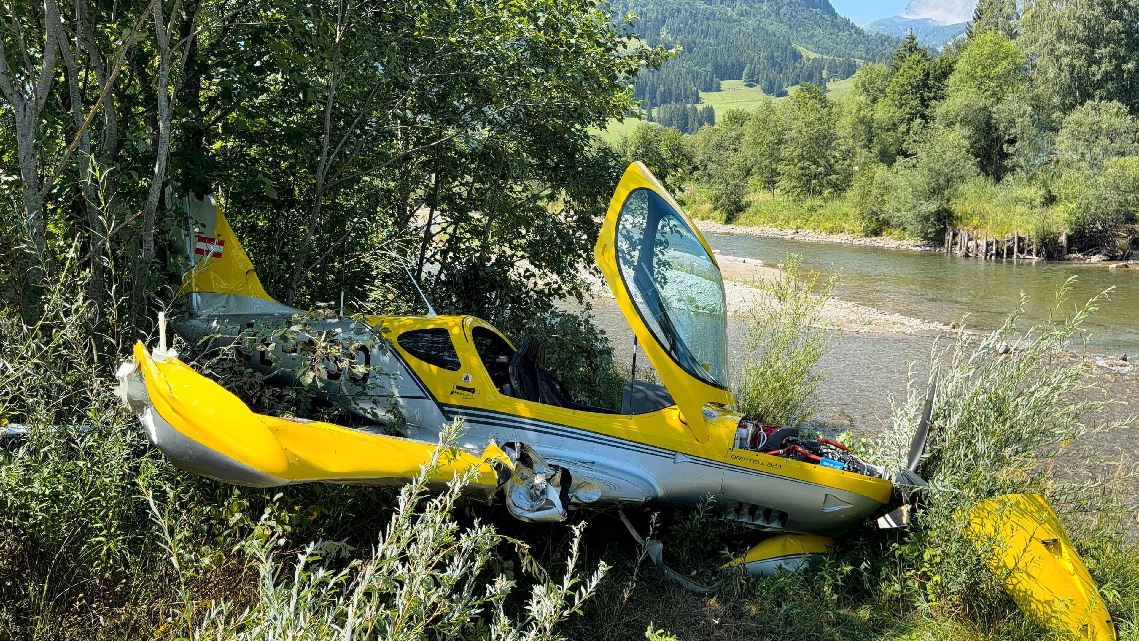 Ein gelbes Kleinflugzeug ist nach einem Unfall am Flussufer und im Gebüsch gelandet.