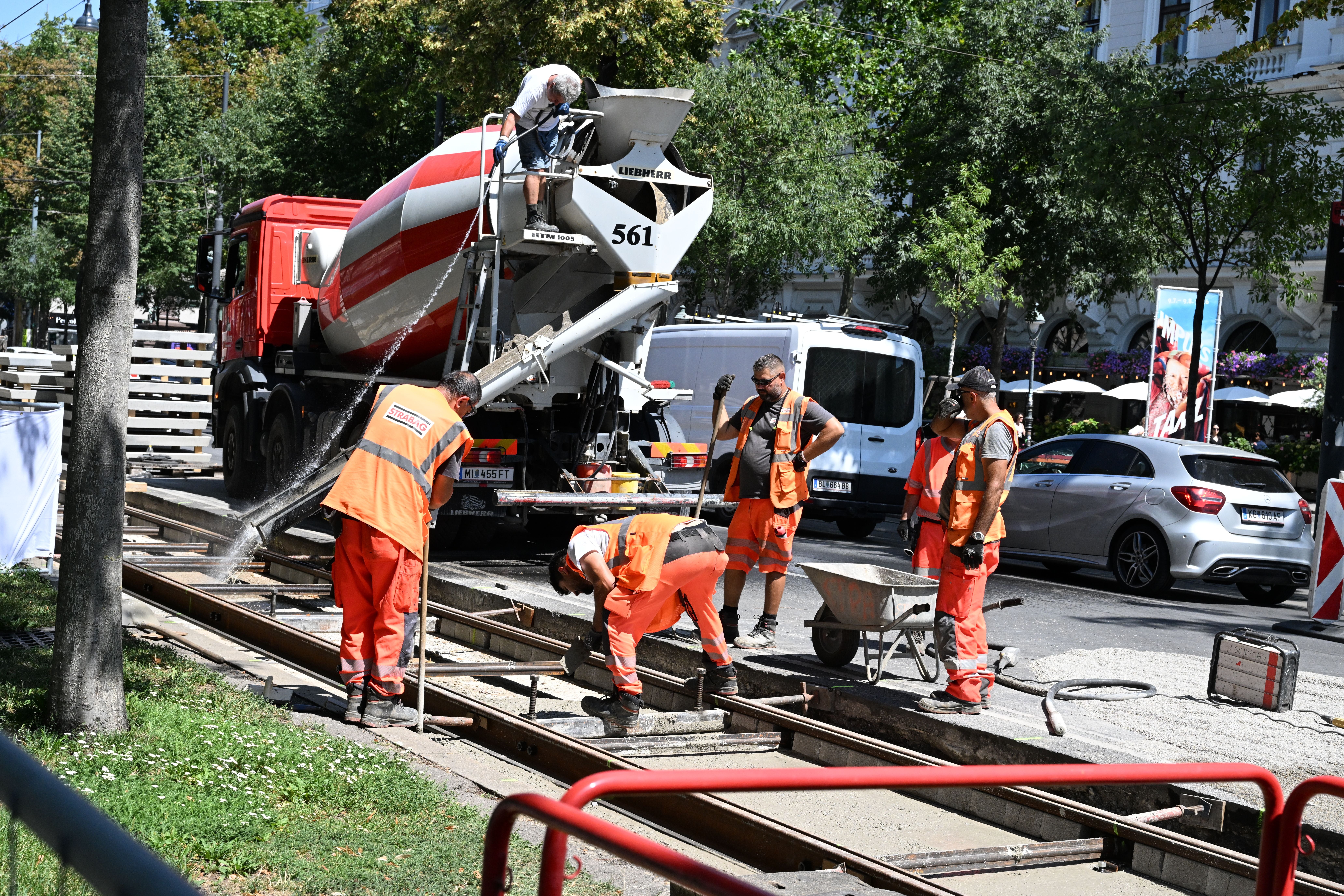 Bauarbeiter gießen Beton in eine Straßenbahnschiene auf einer Baustelle am Rathaus.