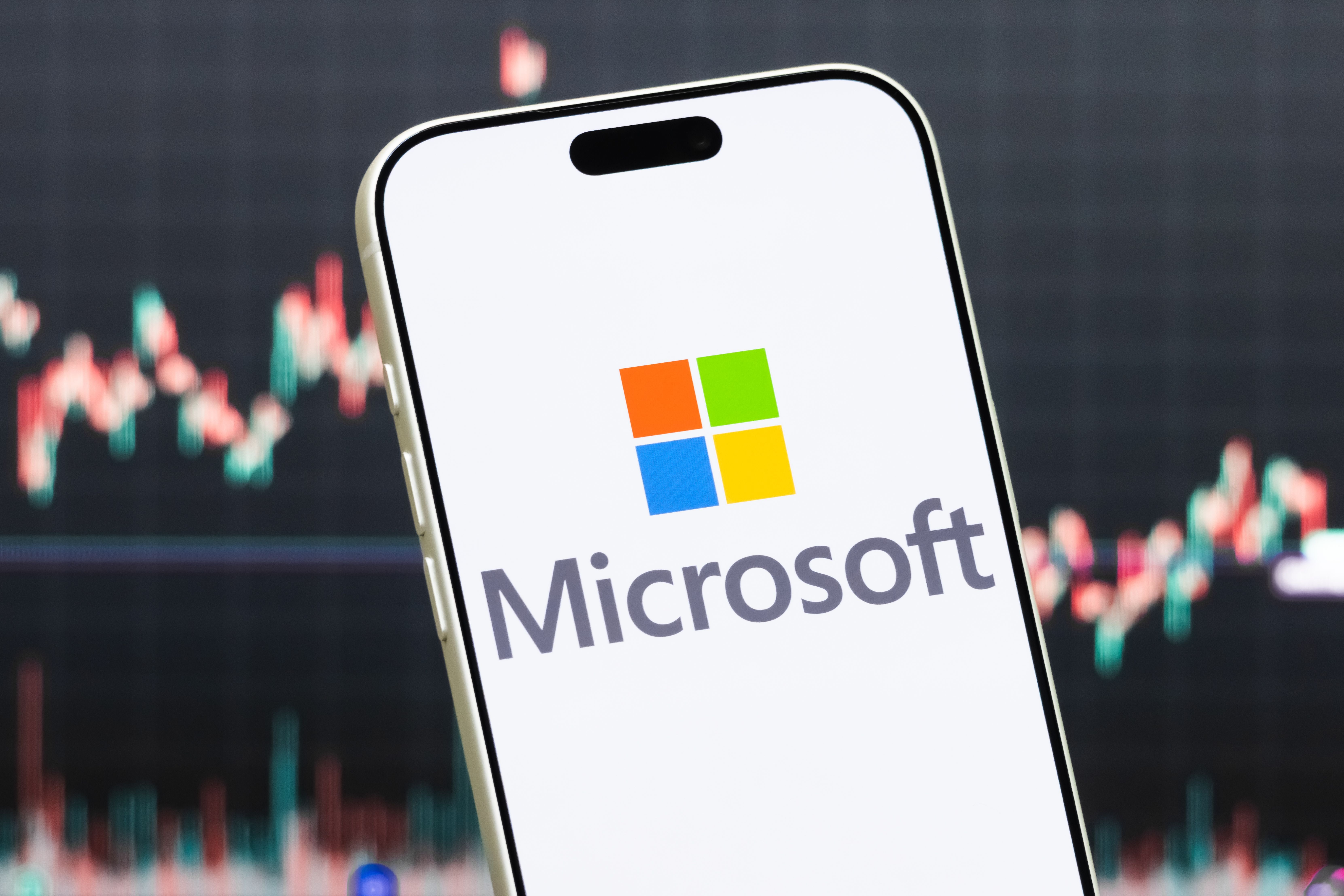 Smartphone mit Microsoft-Logo vor unscharfem Aktienkursdiagramm im Hintergrund.