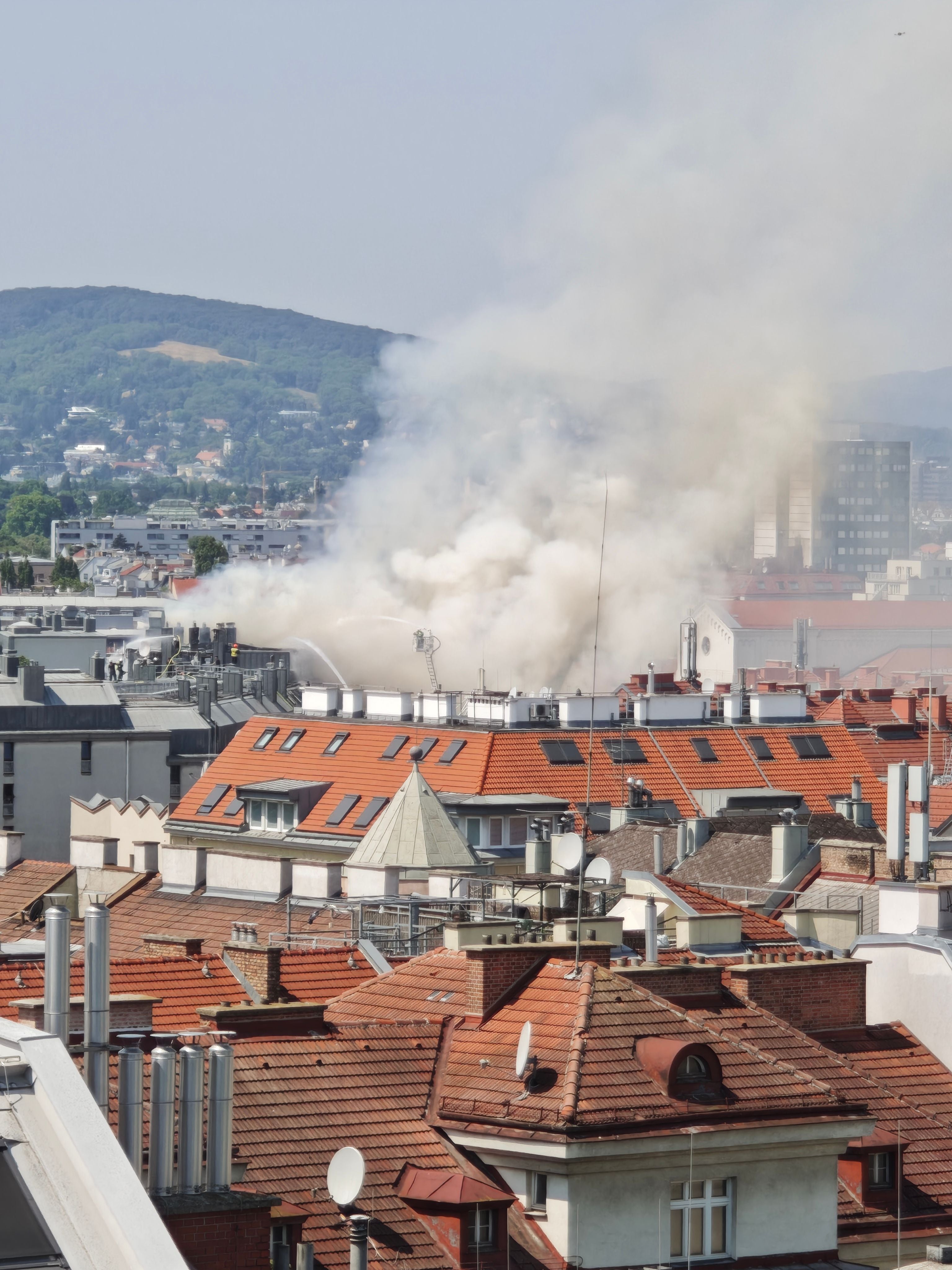 Dichter Rauch steigt über mehreren Häusern mit roten Dächern in Meidling nach einem Dachstuhlbrand auf.
