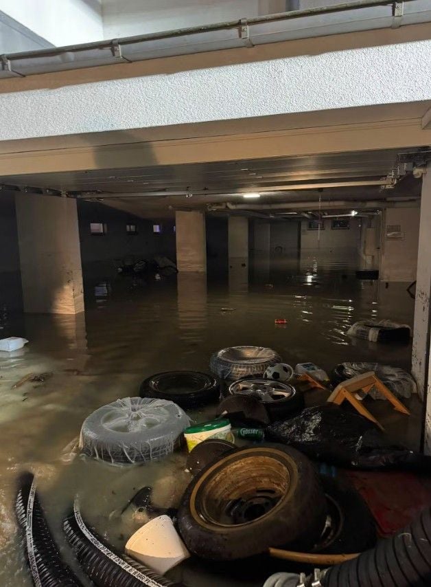 Überflutete Tiefgarage mit schwimmenden Autoreifen und verschiedenen Abfällen im Wasser.