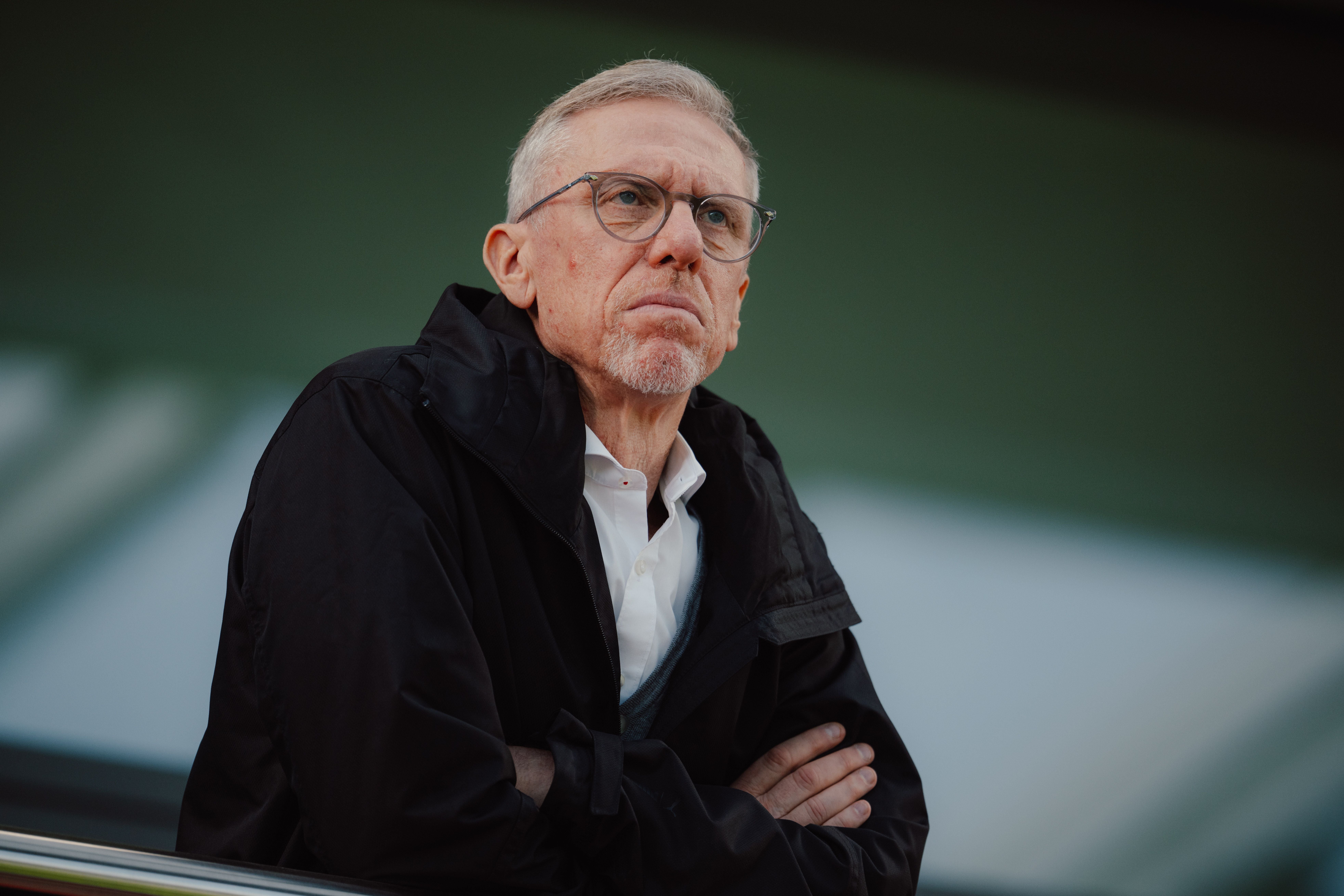 Ein Mann mit Brille und dunkler Jacke steht nachdenklich mit verschränkten Armen.
