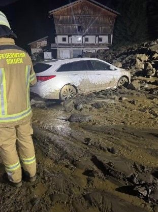 Ein Feuerwehrmann steht vor einem vom Matsch eingeschlossenen Auto nach einem Murenabgang bei Nacht.