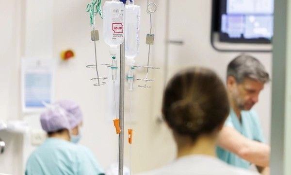 Ärzte und Pflegepersonal arbeiten in einem Krankenhausraum mit Infusionsständern im Vordergrund.