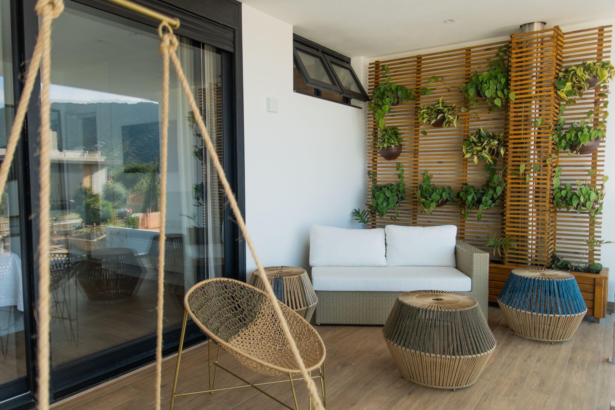 Moderner Balkon mit Sofa, Hängesessel, Rattantischen und vertikaler Holzwand mit Pflanzen.