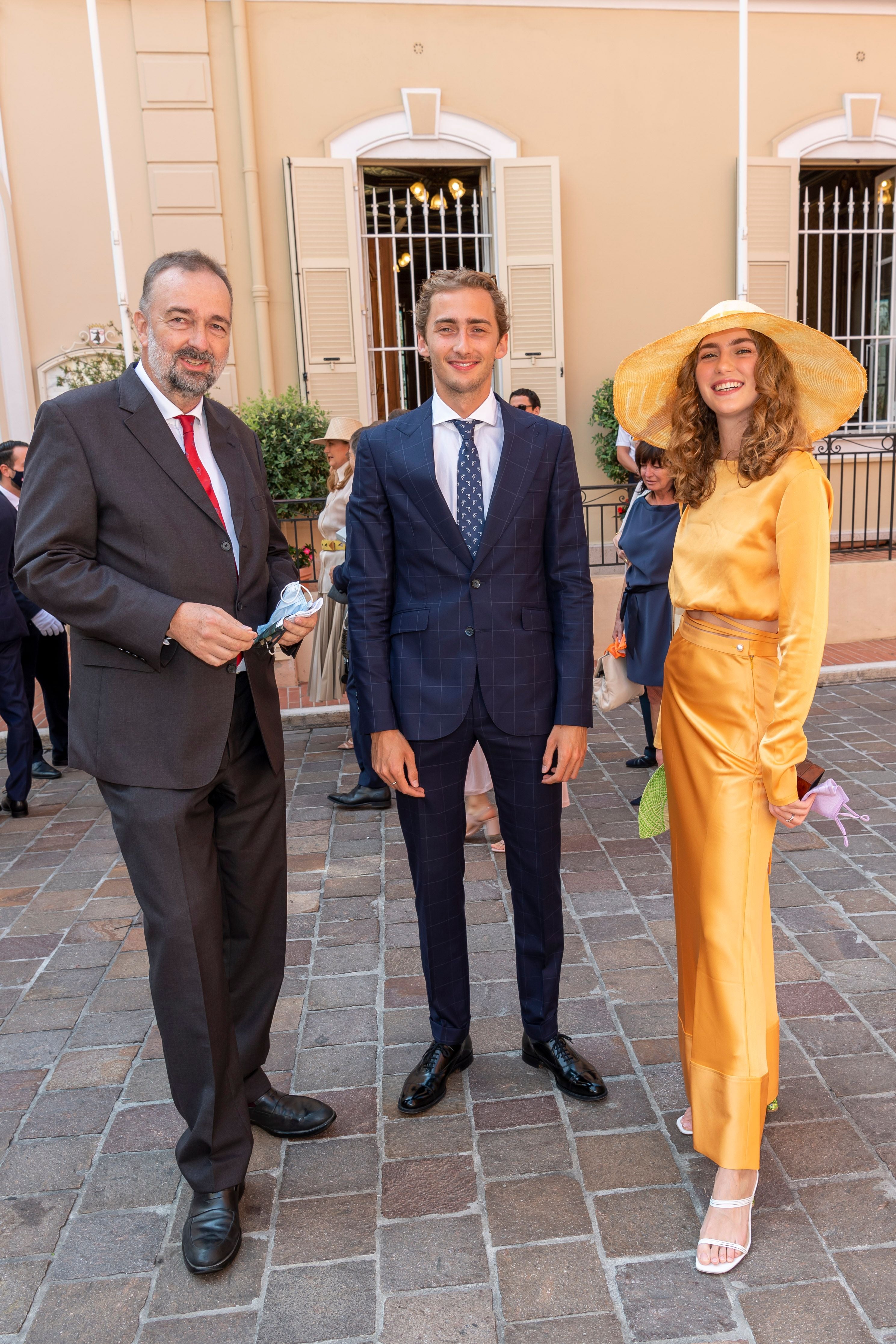 Drei elegant gekleidete Personen posieren draußen vor einem herrschaftlichen Gebäude.