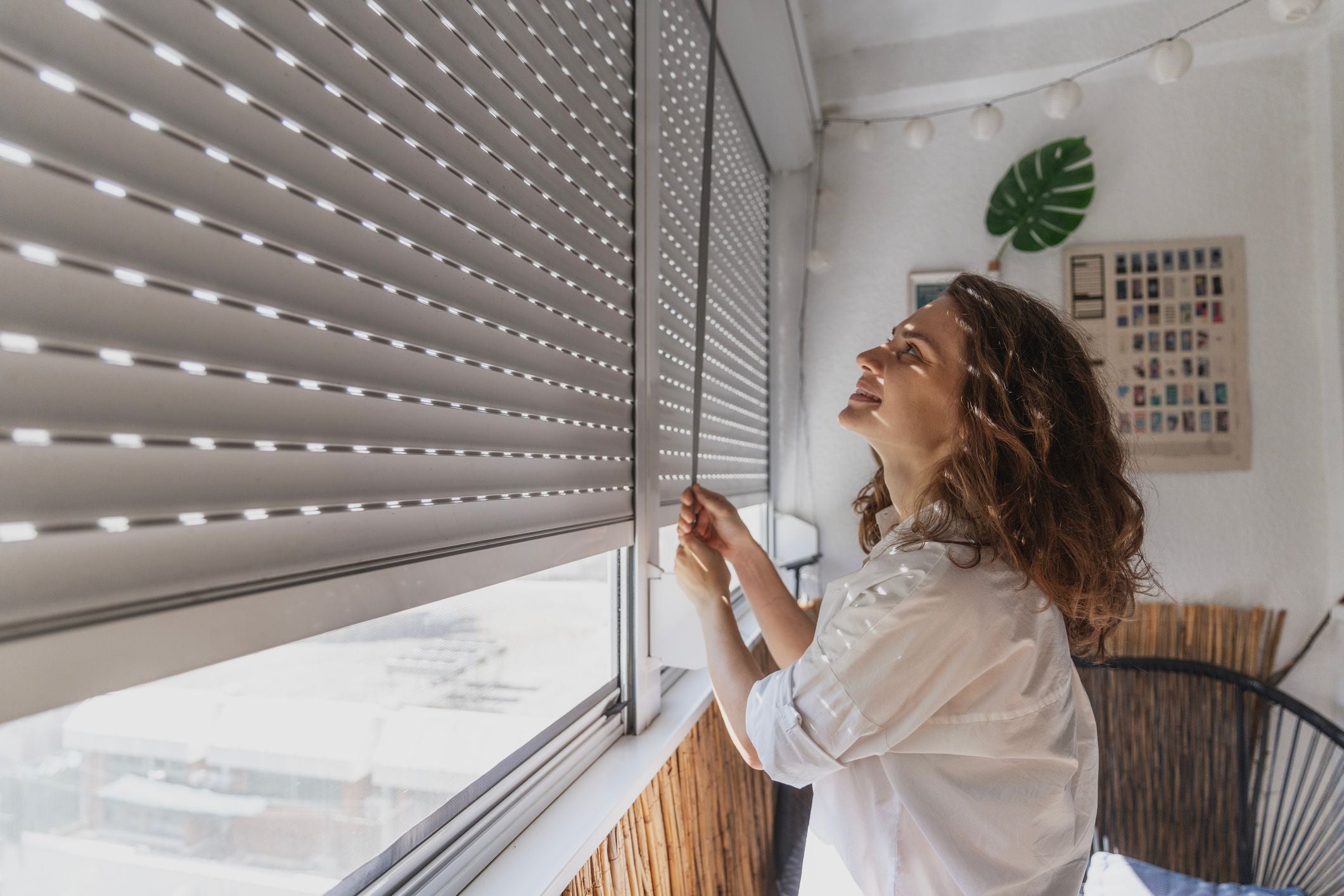 Junge Frau schließt an einem Sommertag Rollläden auf dem Balkon.