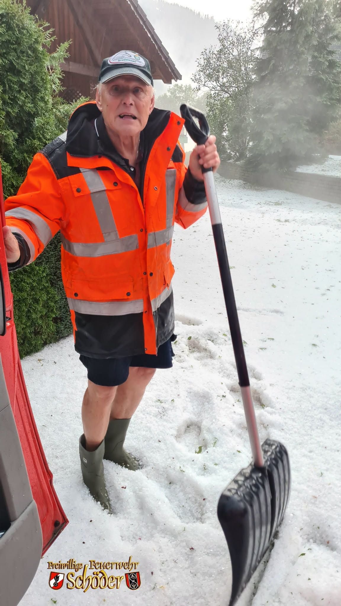 Ein Mann schaufelt in Gummistiefeln und Warnjacke Hagel vor einem Haus in der Steiermark.