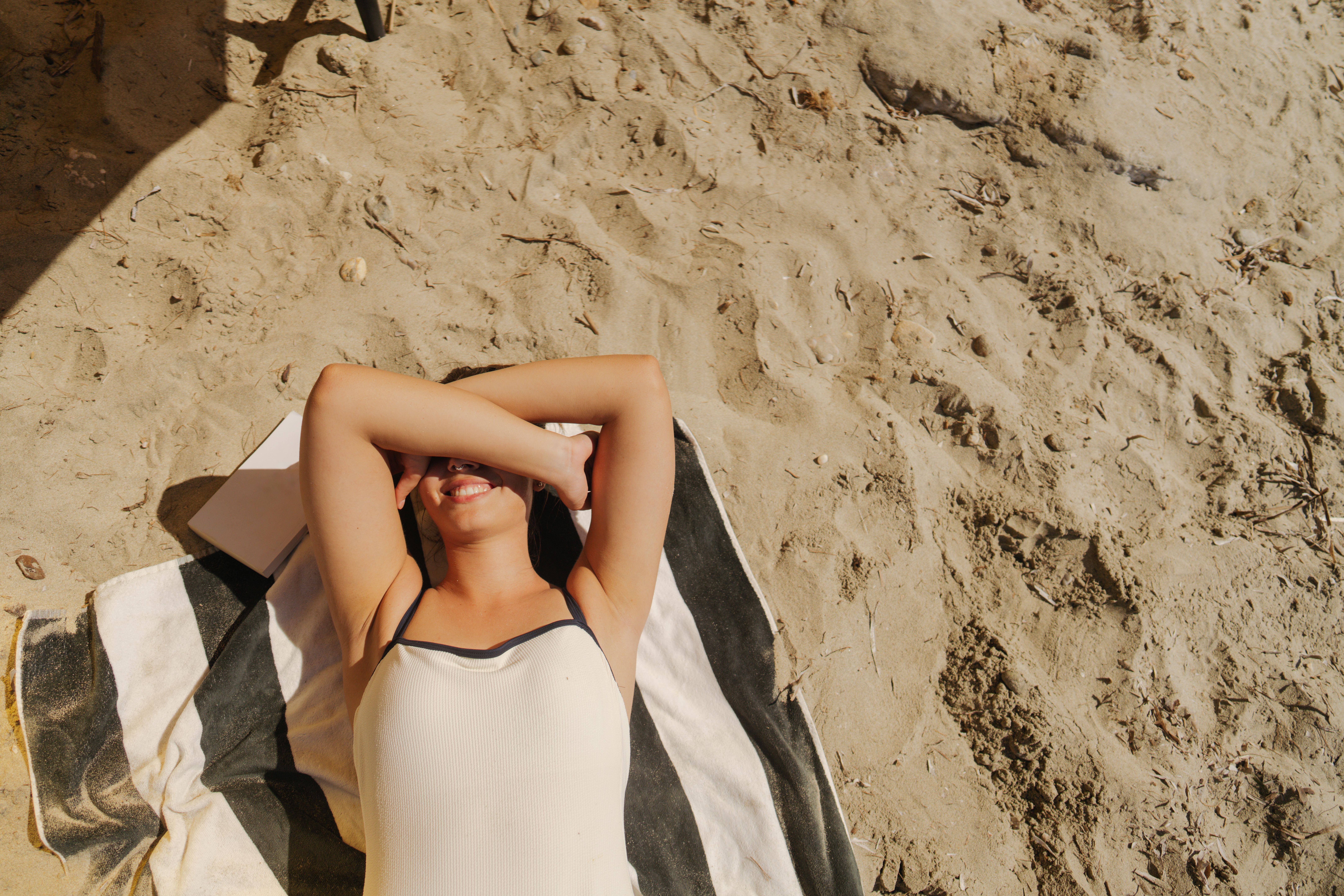 Junge Frau liegt sonnenbadend auf einem Handtuch am Sandstrand.