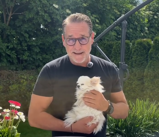 Ein Mann mit Brille hält draußen einen kleinen weißen Hund im Arm.