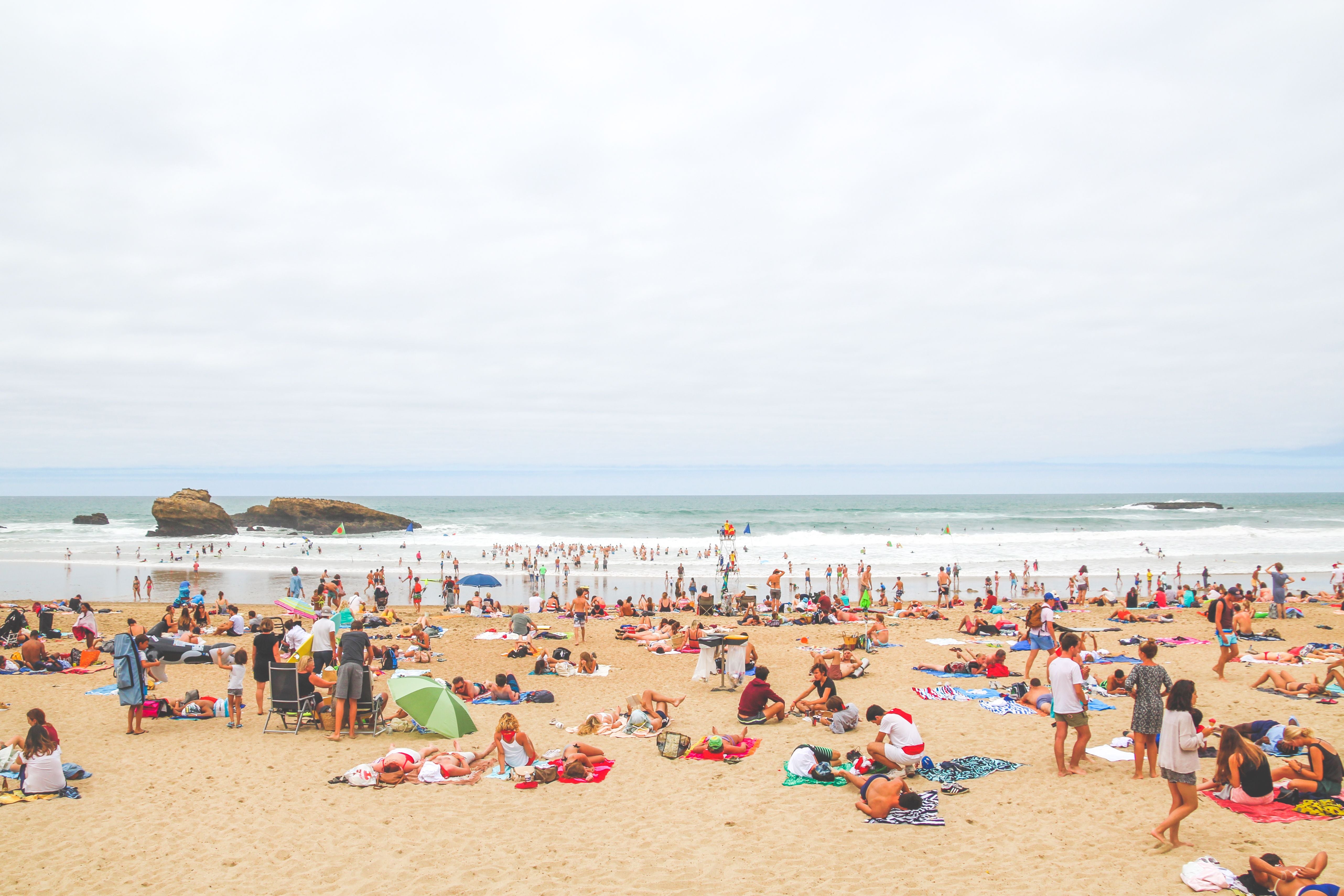 Viele Menschen entspannen am belebten Sandstrand von Biarritz unter wolkigem Himmel.