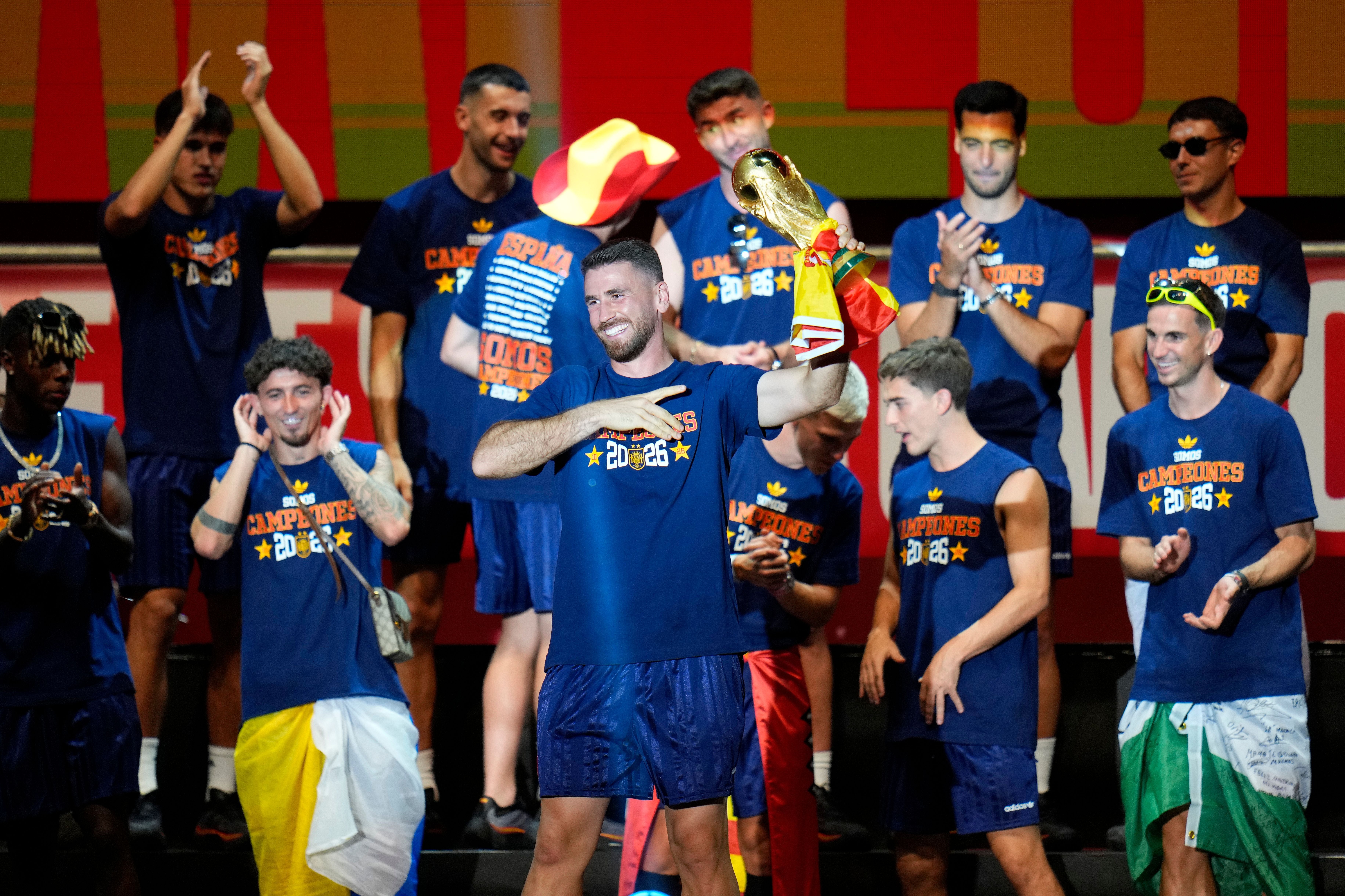 Unai Simon feiert mit dem WM-Pokal 2026 auf einer Bühne, umgeben von jubelnden Teamkollegen.