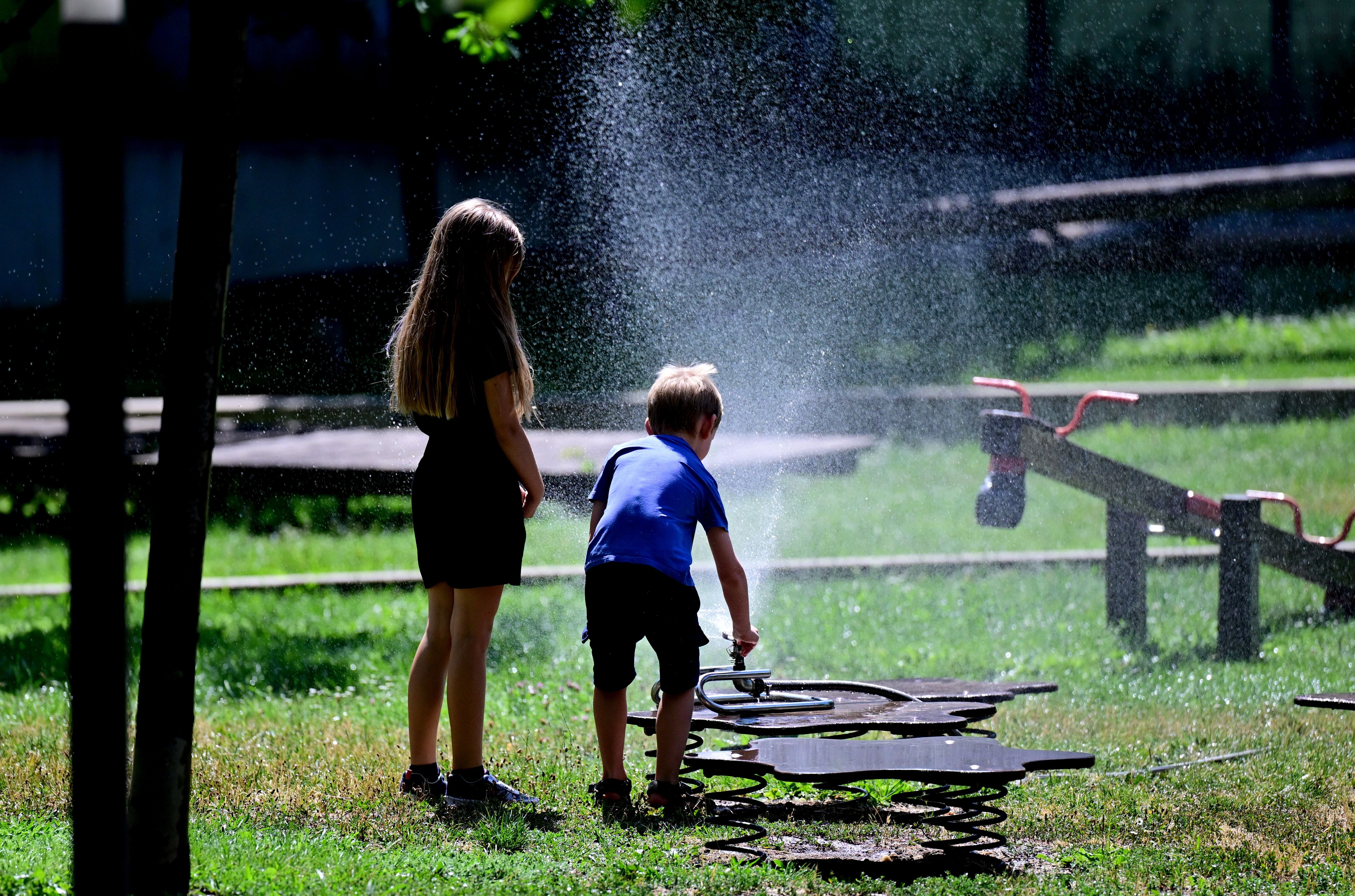 Zwei Kinder kühlen sich auf einem Spielplatz in Wien unter einer Bewässerungsanlage ab.