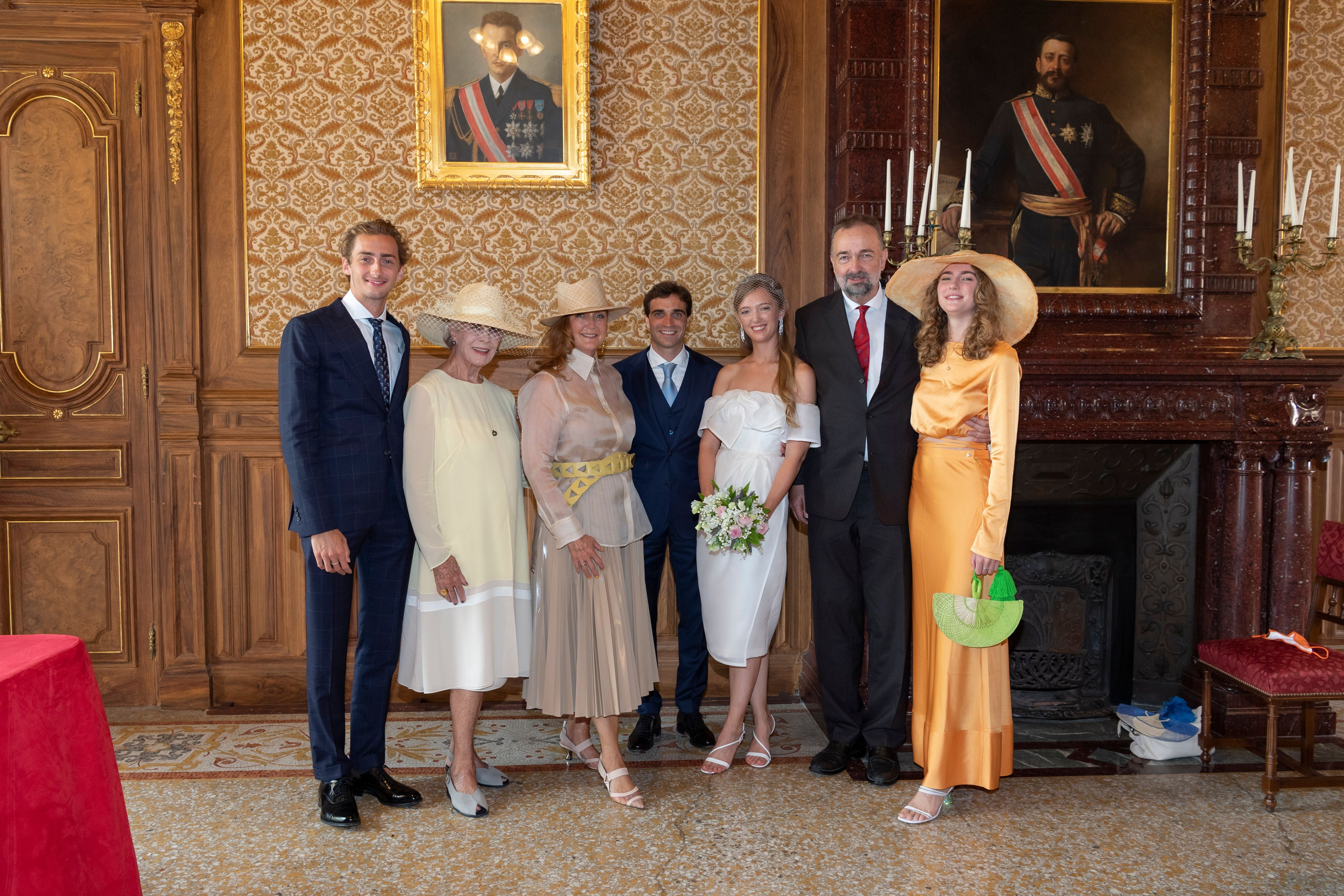 Sieben elegant gekleidete Menschen posieren bei einer Hochzeit in einem prunkvollen Raum.
