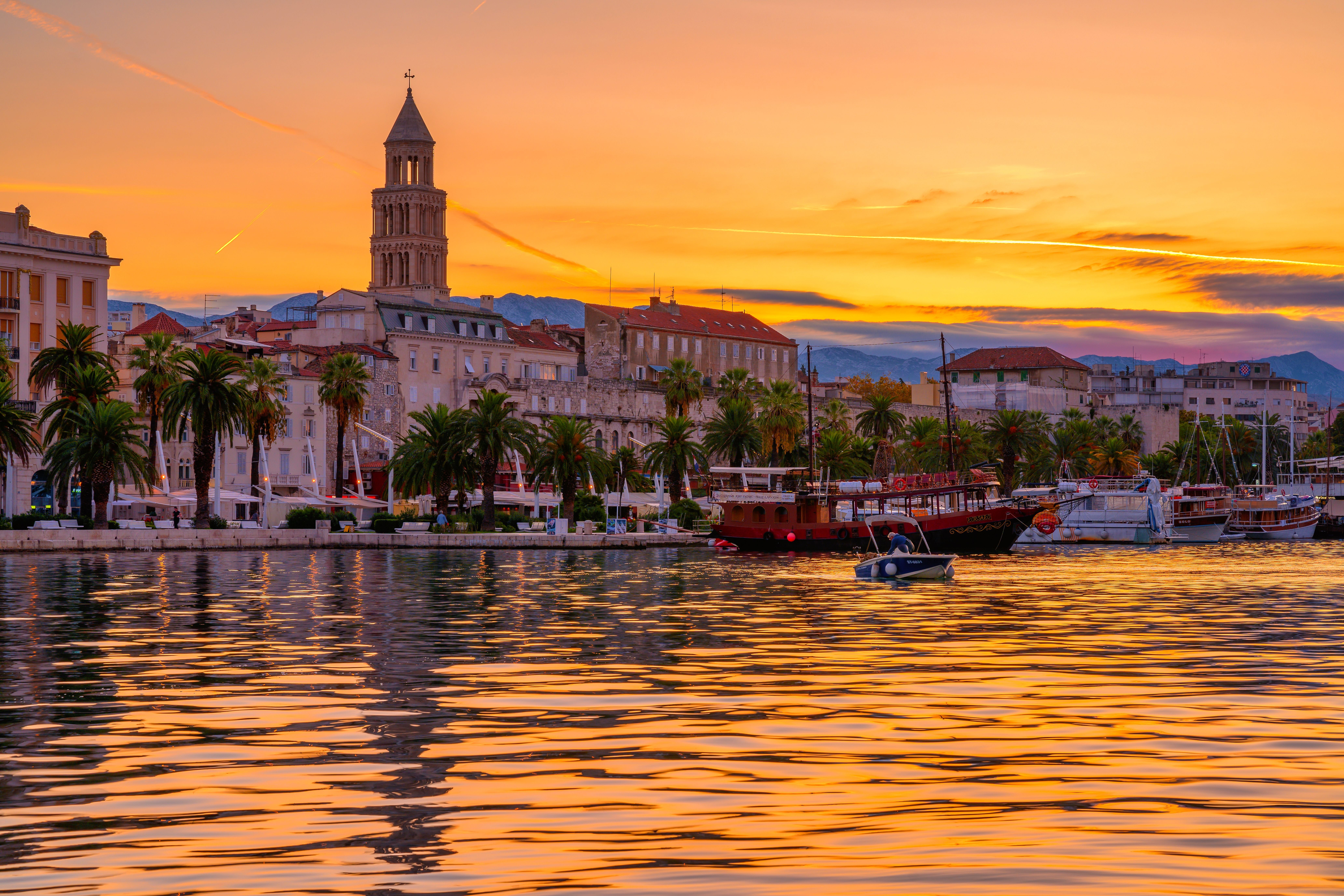 Die Altstadt von Split in Kroatien bei Sonnenaufgang mit Booten und Palmen am Wasser.
