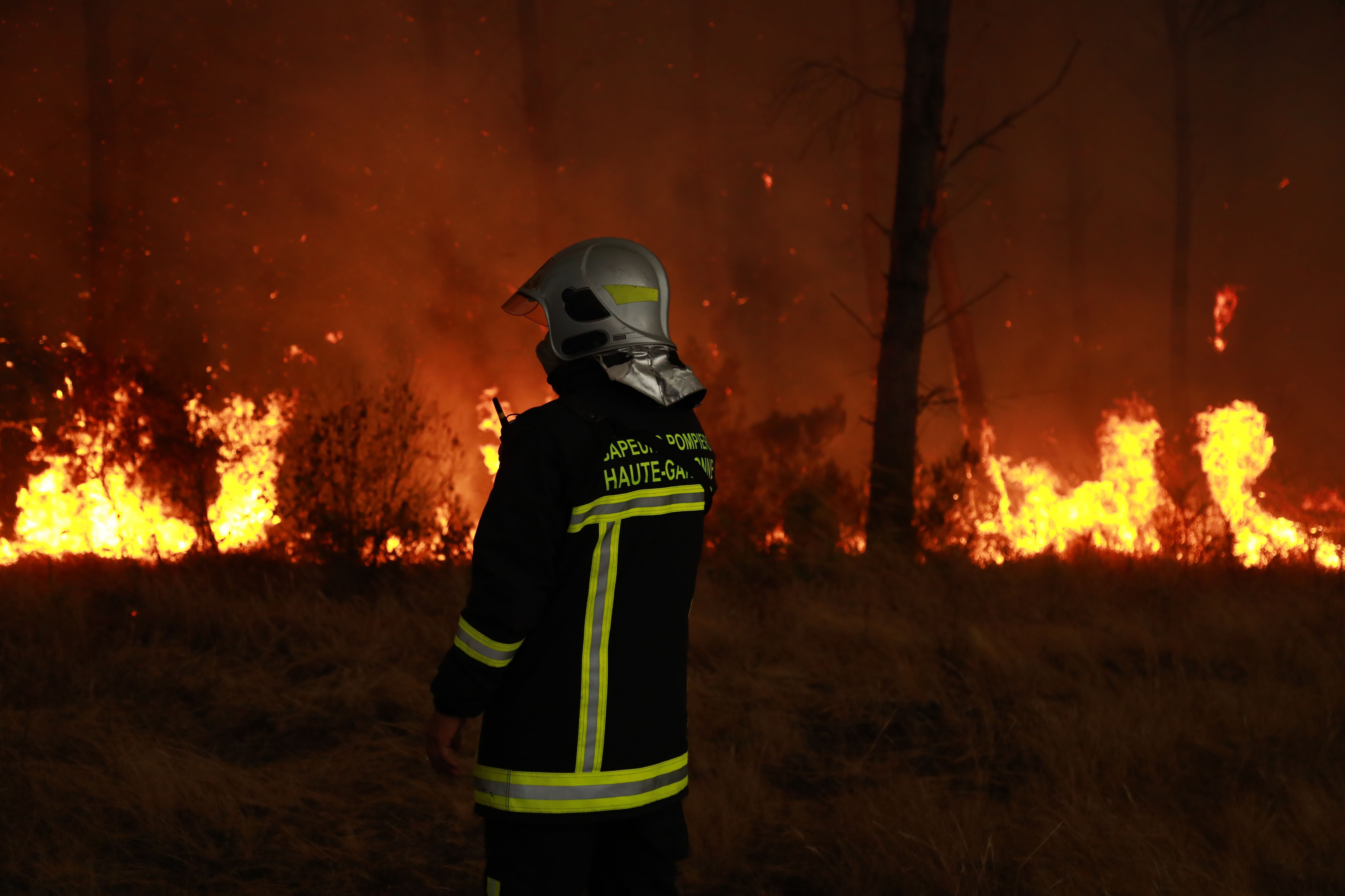 Ein Feuerwehrmann steht vor einem brennenden Wald bei nächtlichem Großeinsatz gegen ein Feuer.