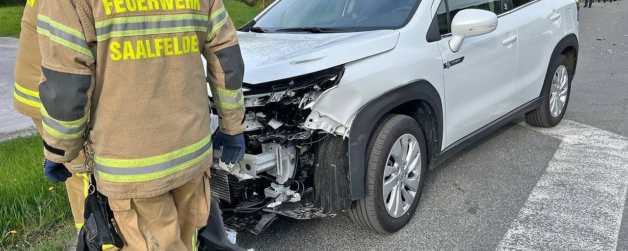 Feuerwehrleute stehen neben einem Auto mit stark beschädigter Front nach einem Unfall.