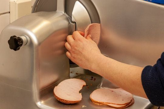 Eine Hand schneidet Extrawurst mit einer Aufschnittmaschine in Scheiben.