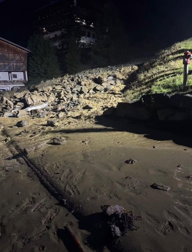 Bei Nacht beleuchteter Hang mit Erdrutsch und Geröll vor Gebäuden in Tirol.